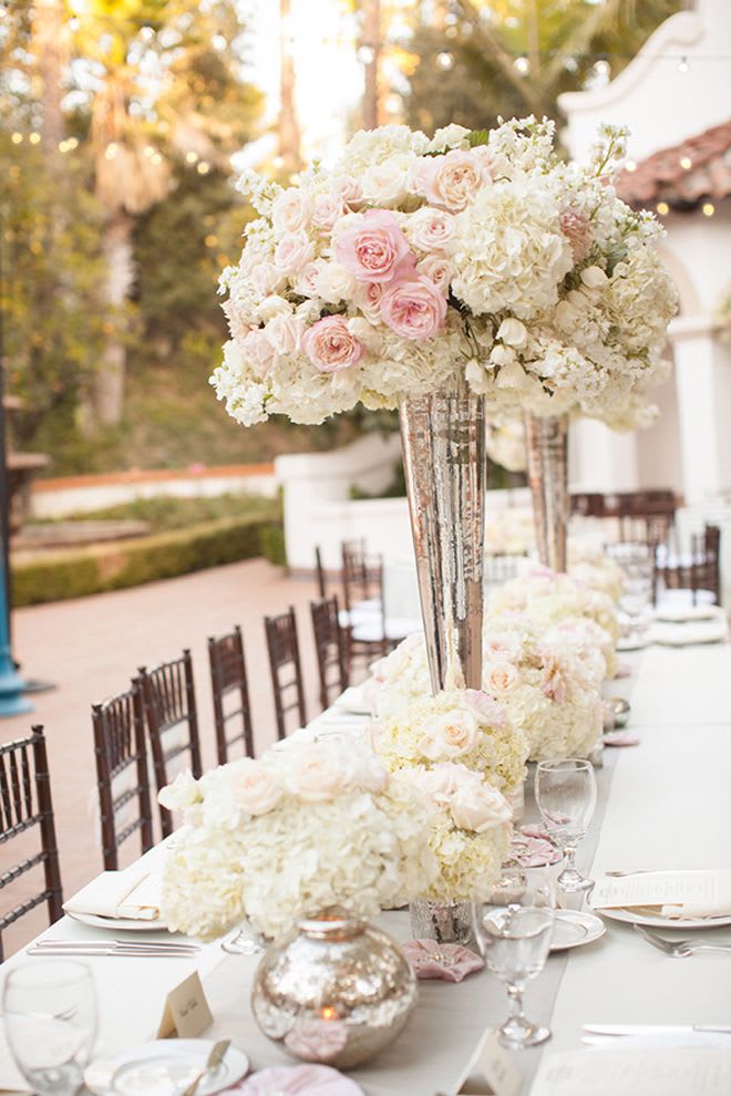Tall centerpiece of pale pink roses and white flowers in a mirrored vase