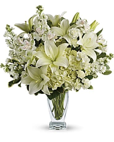 White lilies and pale flowers arranged in a clear glass vase