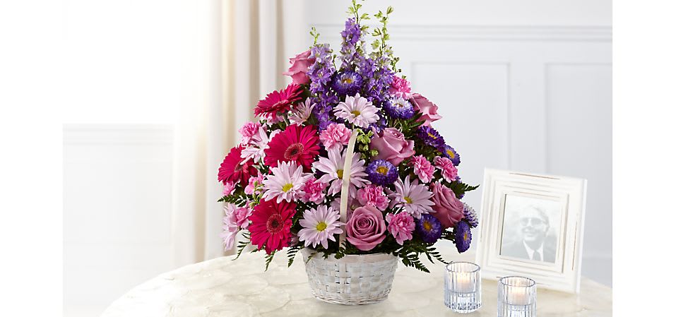 Mixed pink, purple, and white flowers in a white basket on a table