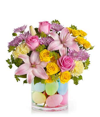 Pink and yellow flowers in a clear vase with pastel egg decorations