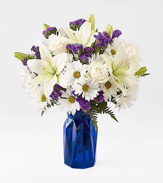 White lilies and daisies with purple filler in a blue vase