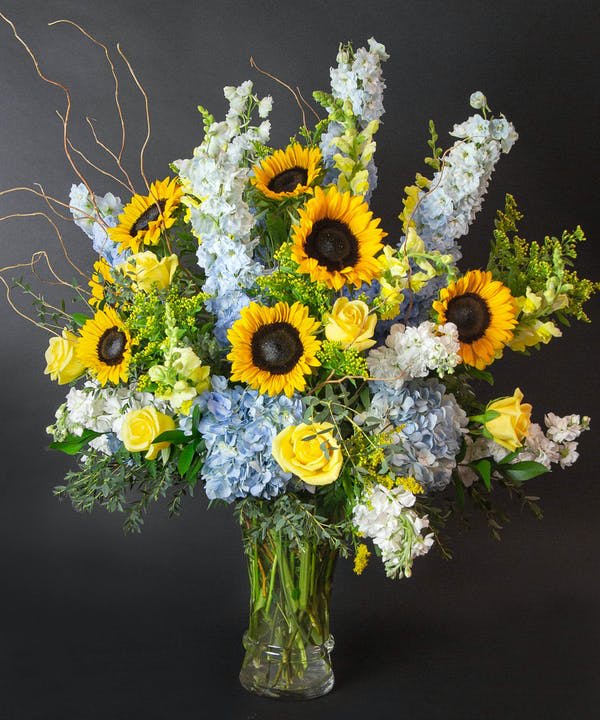 Sunflowers, blue hydrangeas, and yellow roses in a glass vase