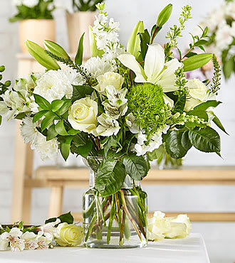 White floral arrangement in a clear glass vase with lilies and roses