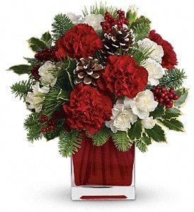 Red and white floral arrangement in a clear vase with pinecones and berries