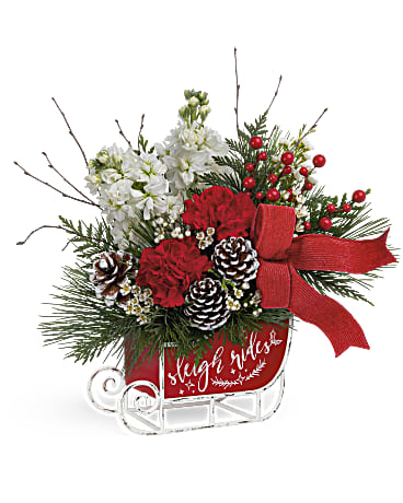 Christmas arrangement with red carnations, white flowers, pinecones, and a red bow in a sleigh container