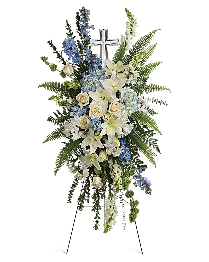 Standing floral spray with white lilies, cream roses, and blue flowers on an easel