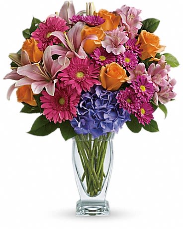 Mixed bouquet of pink, orange, and blue flowers in a clear glass vase