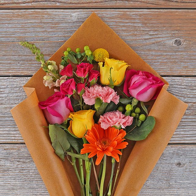 Bouquet of pink and yellow roses with an orange gerbera daisy in brown paper