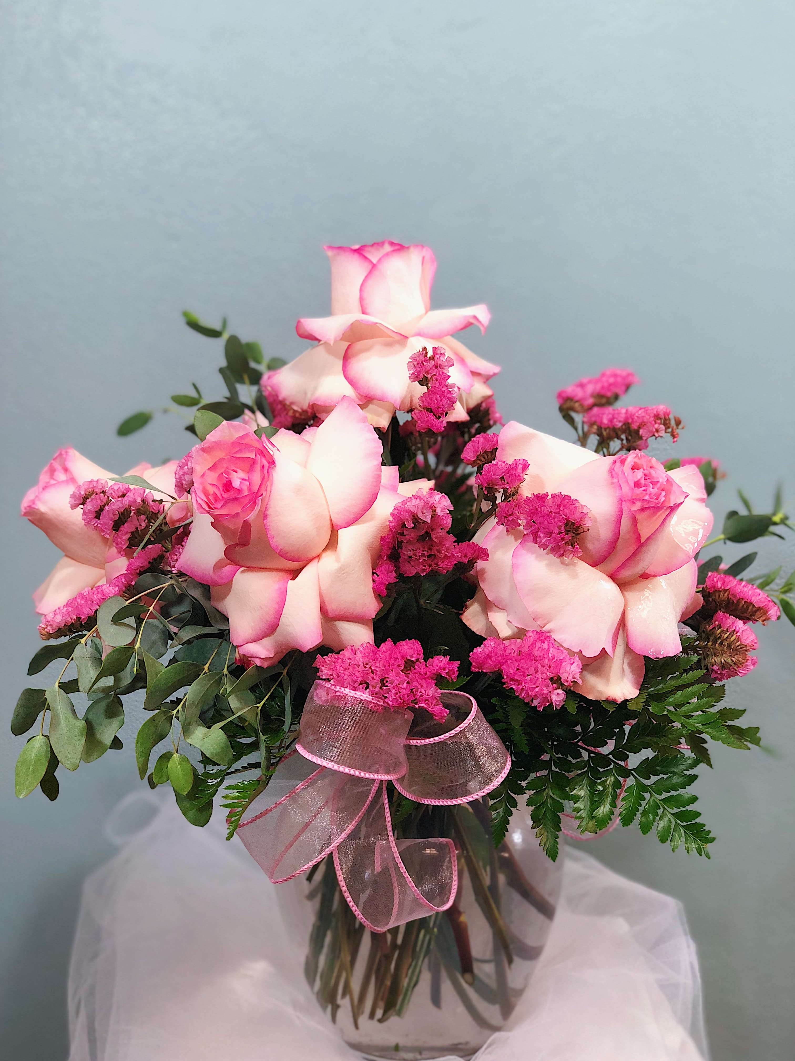 Pink-tipped white roses with bright pink filler flowers in a clear glass vase with a pink ribbon.