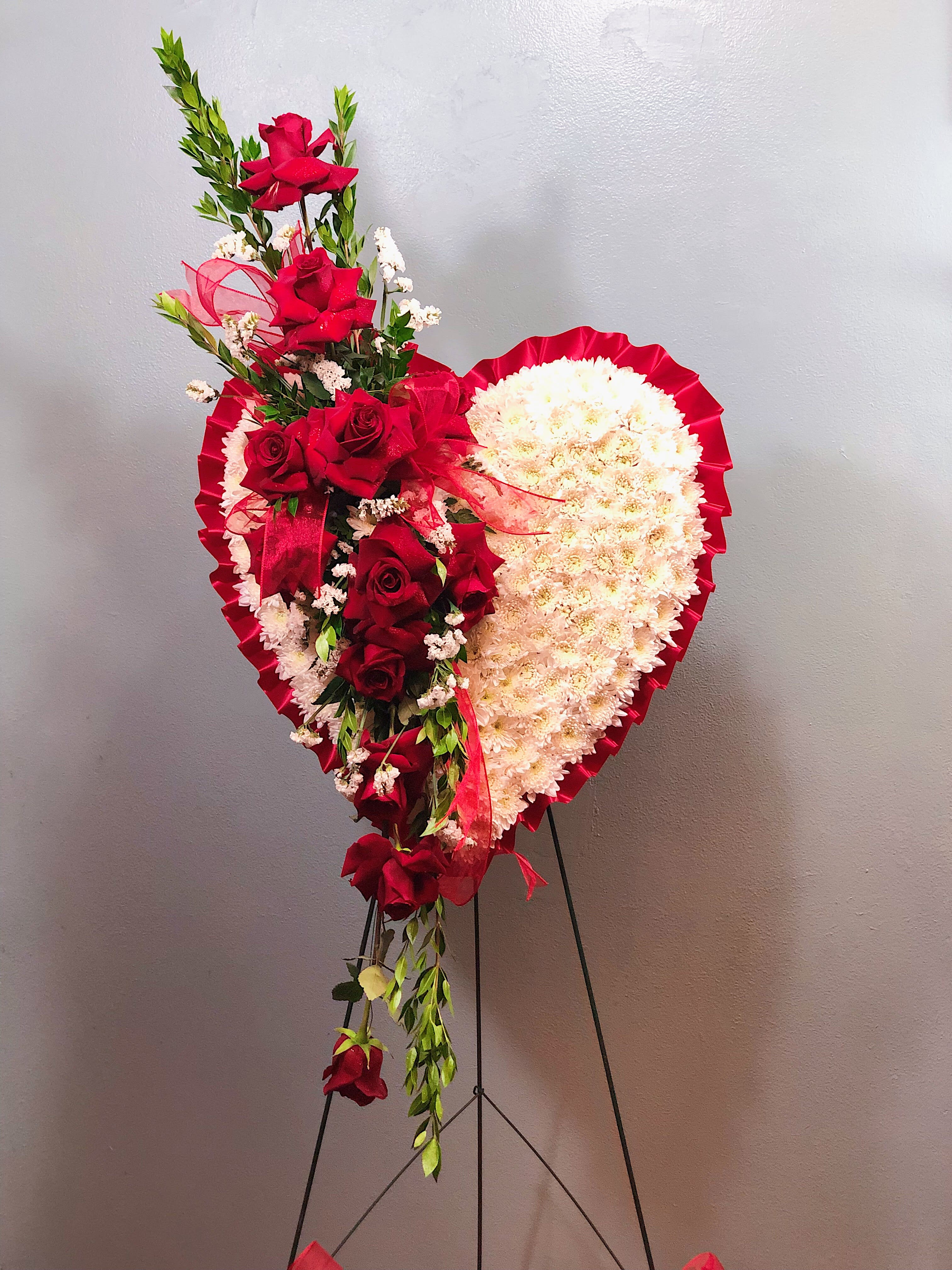 Bleeding Heart Spray  - The loss of a loved one is heartbreaking and sometimes we do not have the words to express it. The Bleeding Heart Spray speaks for your heart. It conveys the pain that you feel, but also the love. The arrangement part of the Bleeding Heart Spray contains one dozen of red roses and is filled with white statice and long green myrtle. The heart is a foam-covered heart edge with red ribbon and covered with white cushions. Red sheer ribbon is added in the arrangement and at the bottom of the stand for the final touches. 