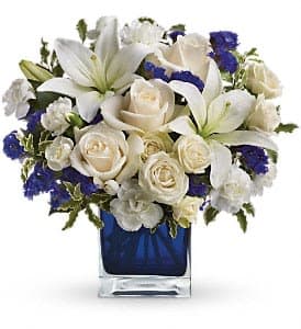 White lilies and roses with blue accents in a glass vase