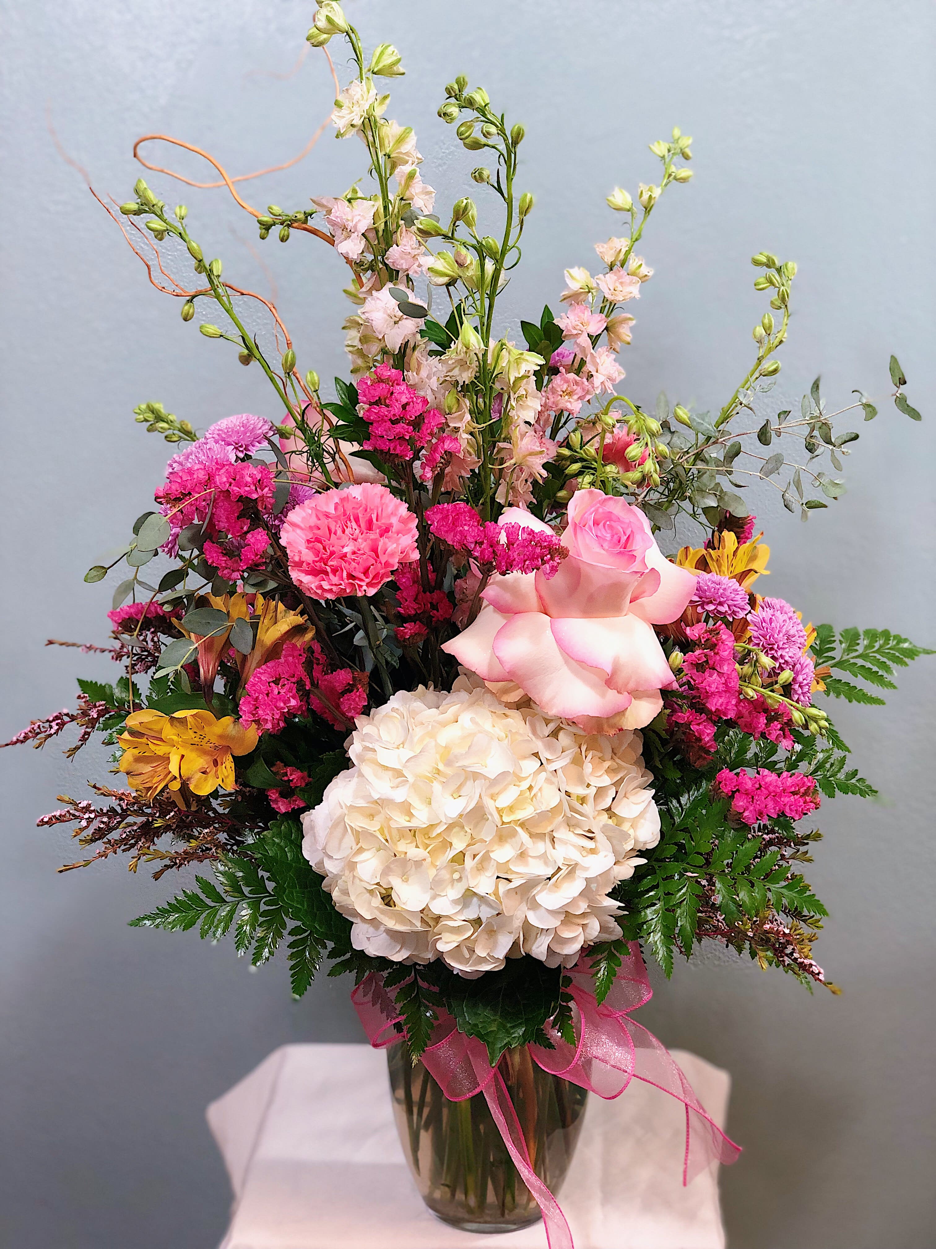Mixed pink and cream bouquet in a glass vase with a pink ribbon