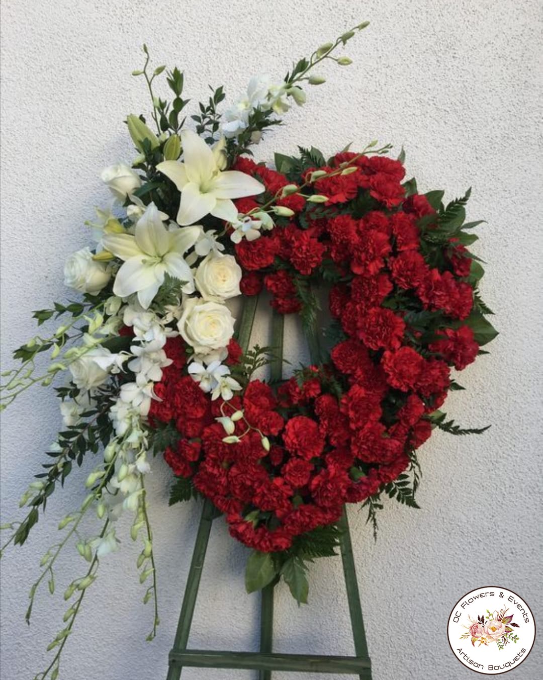 Heart-shaped floral wreath with red carnations and white lilies on an easel