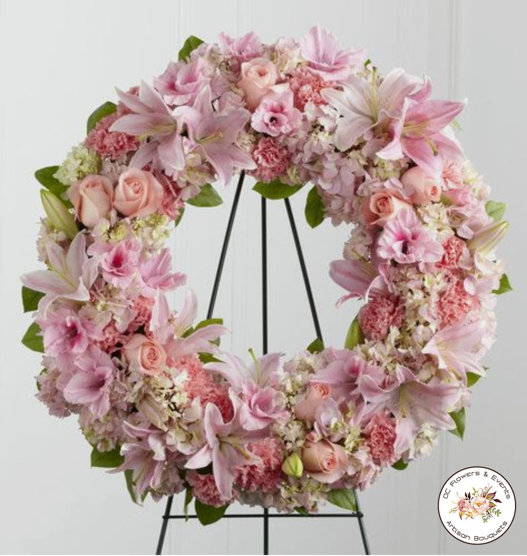 Pink and white floral wreath of lilies, roses, carnations, and hydrangeas on a black stand