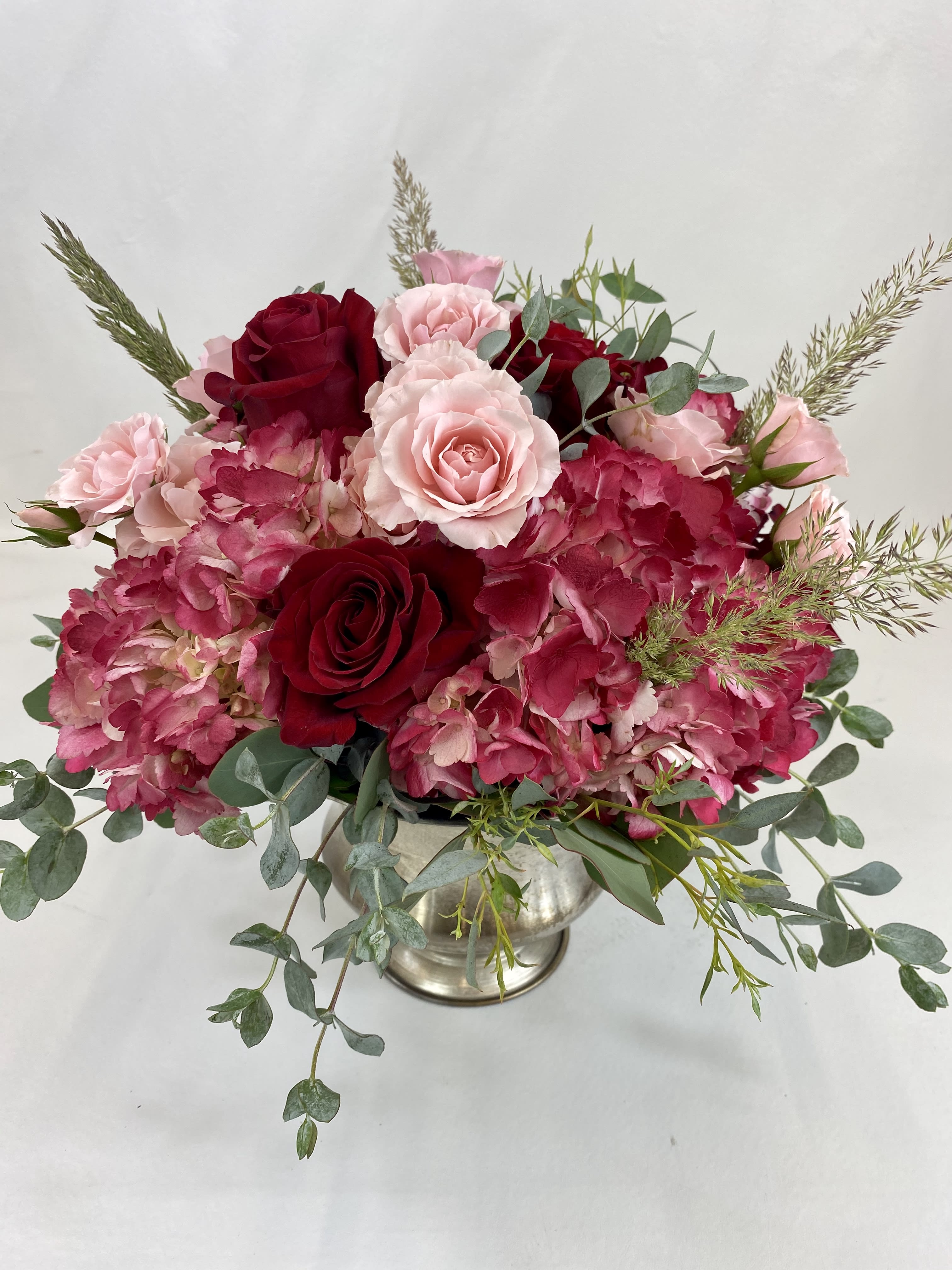 Whimsical  - Elegant flower arrangement with red hydrangeas, roses, spray roses and mix of greenery in a silver metal vase.