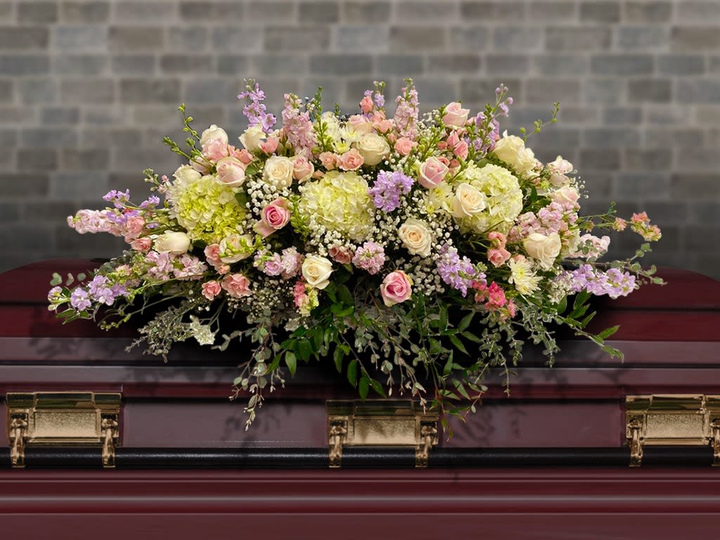 Pastel pink and cream casket spray with roses and hydrangeas on a dark wood casket