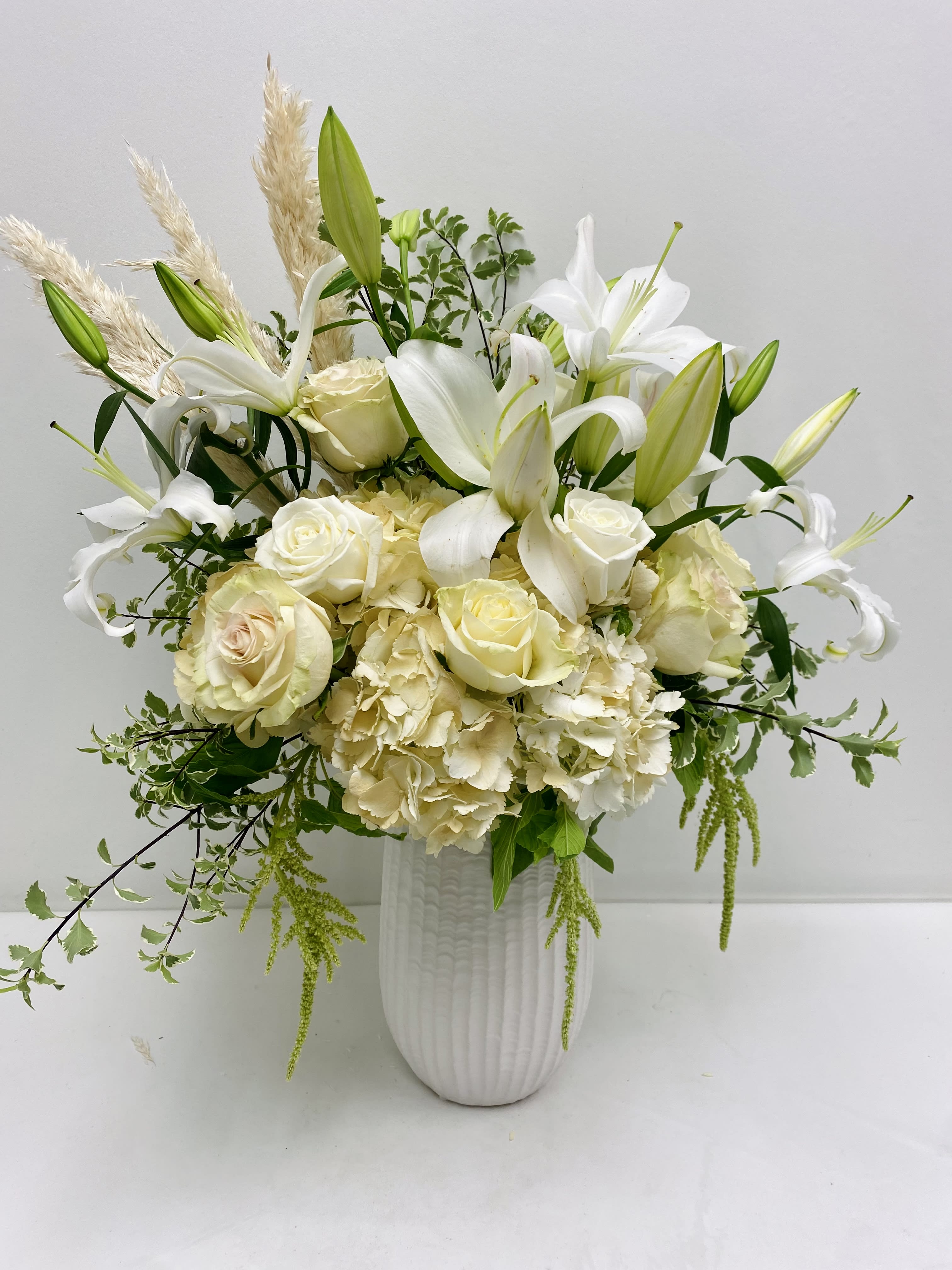 White lilies and roses arranged in a tall white vase