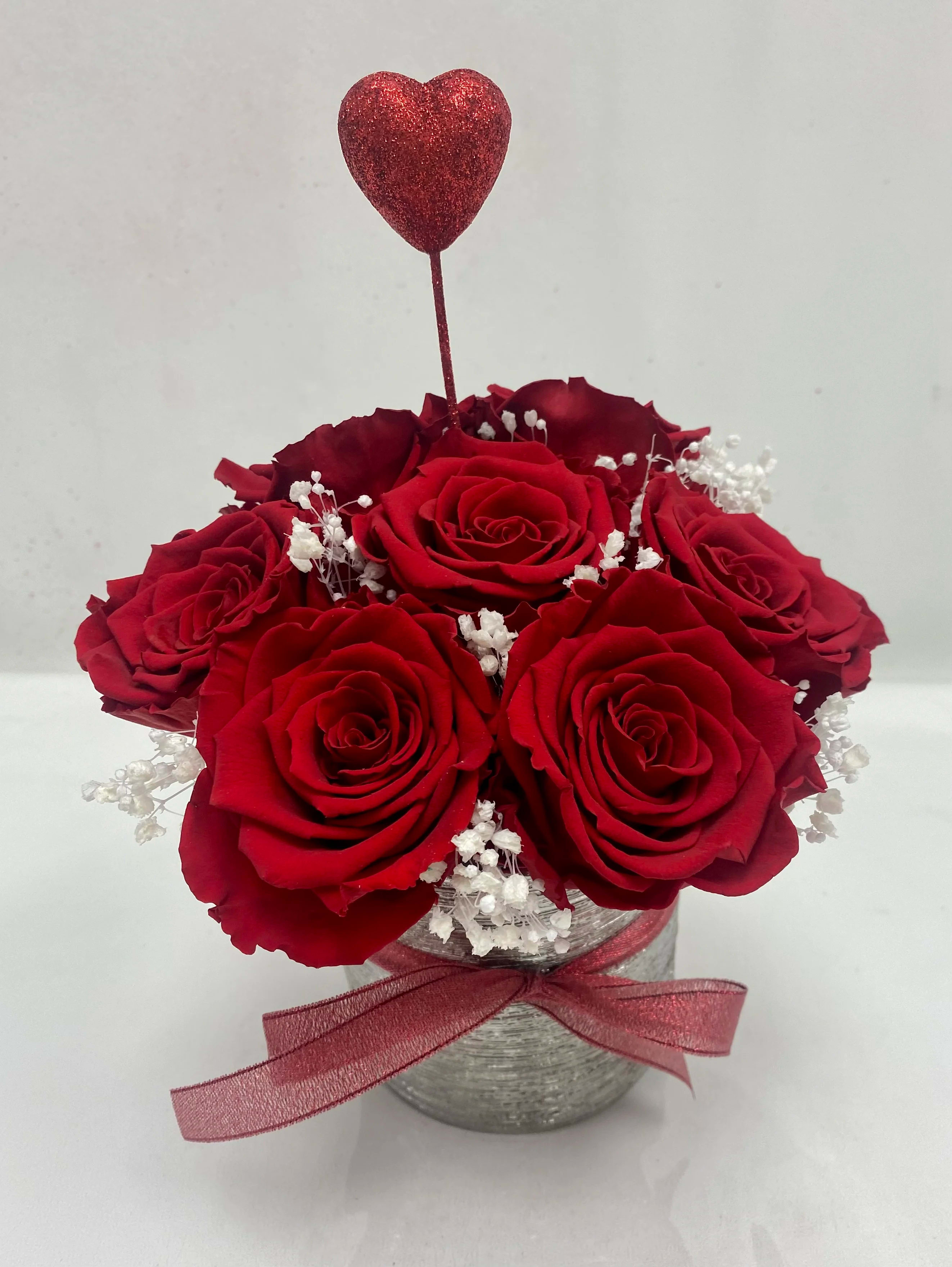 Red roses in a silver vase with a glitter heart pick