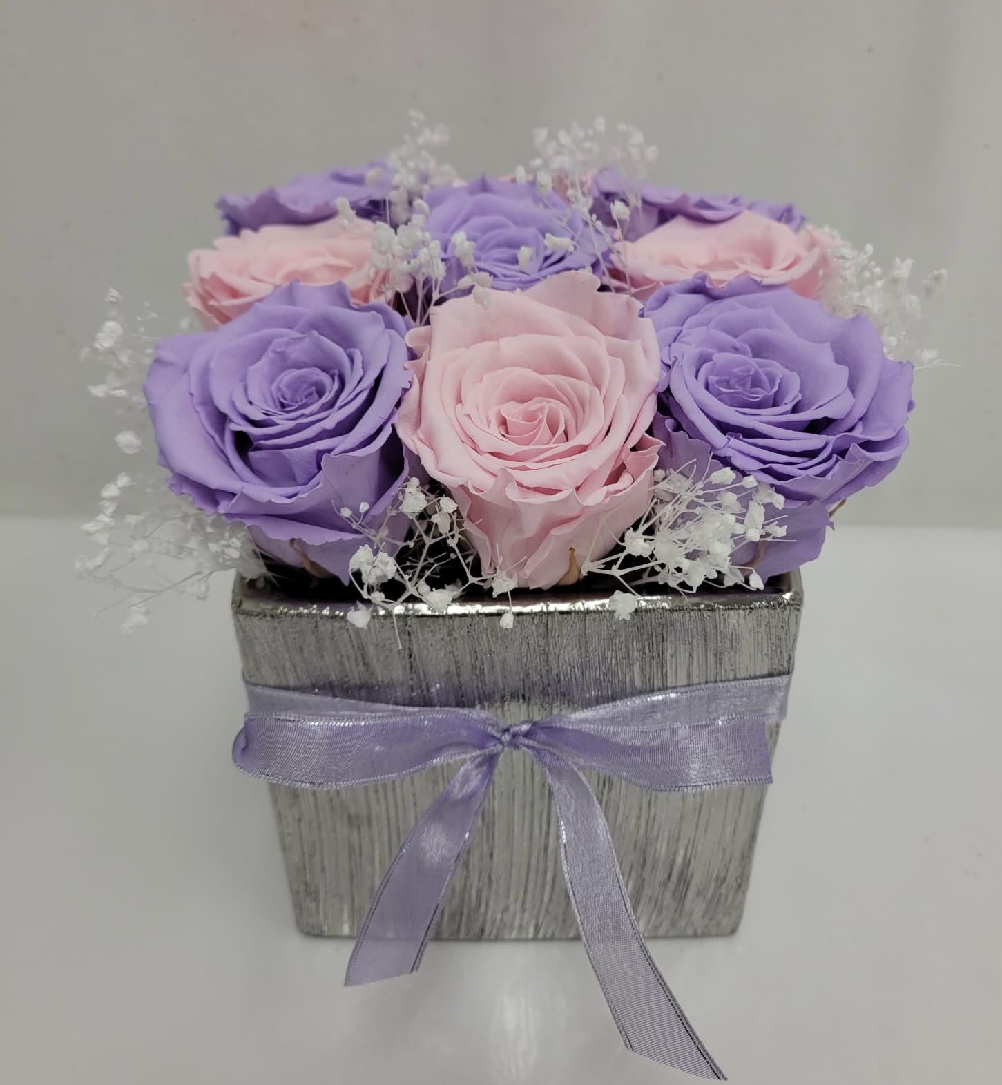 Pink and lavender roses in a silver square box with a purple ribbon
