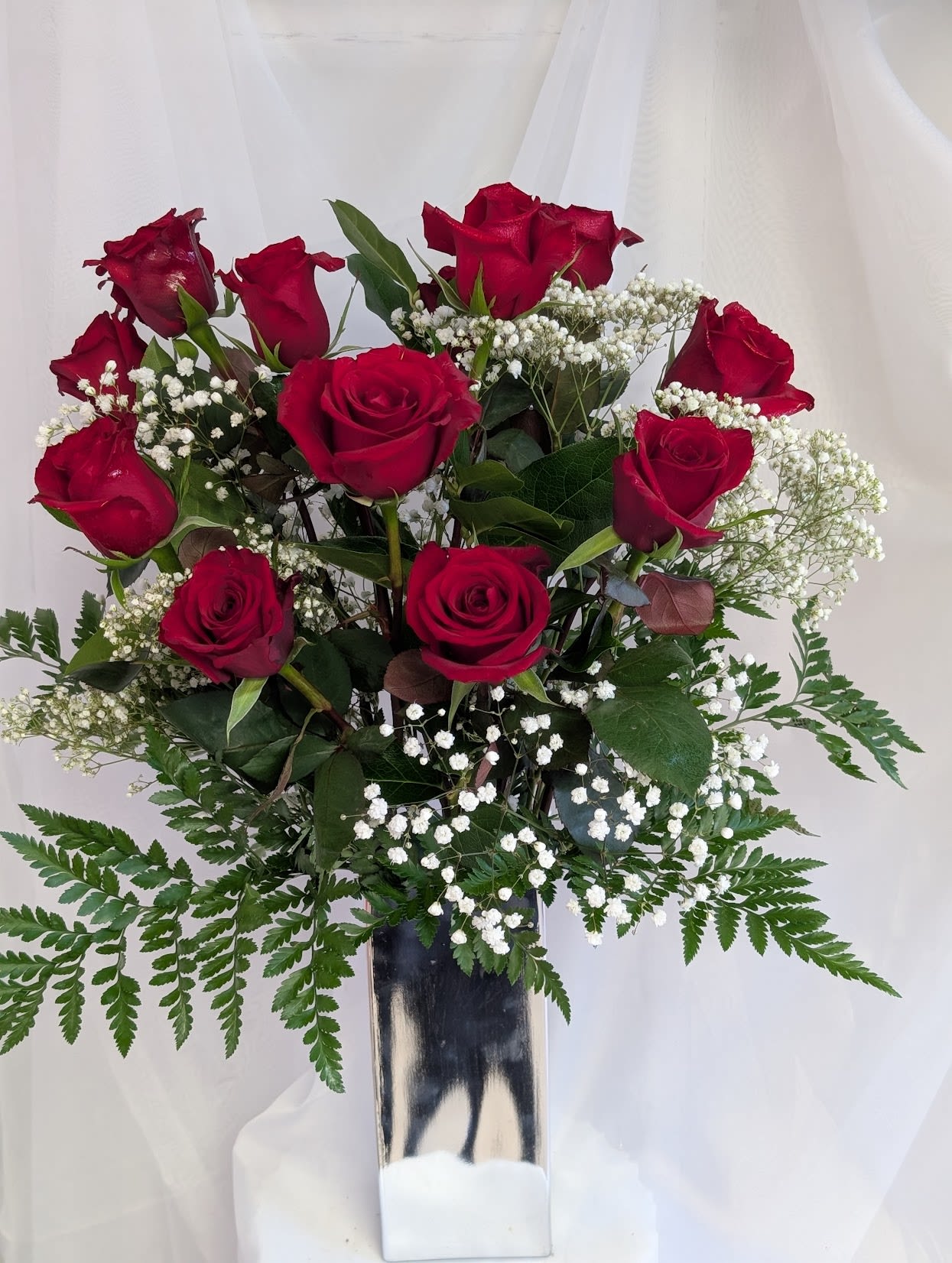 Red roses arranged in a tall silver vase with white baby's breath