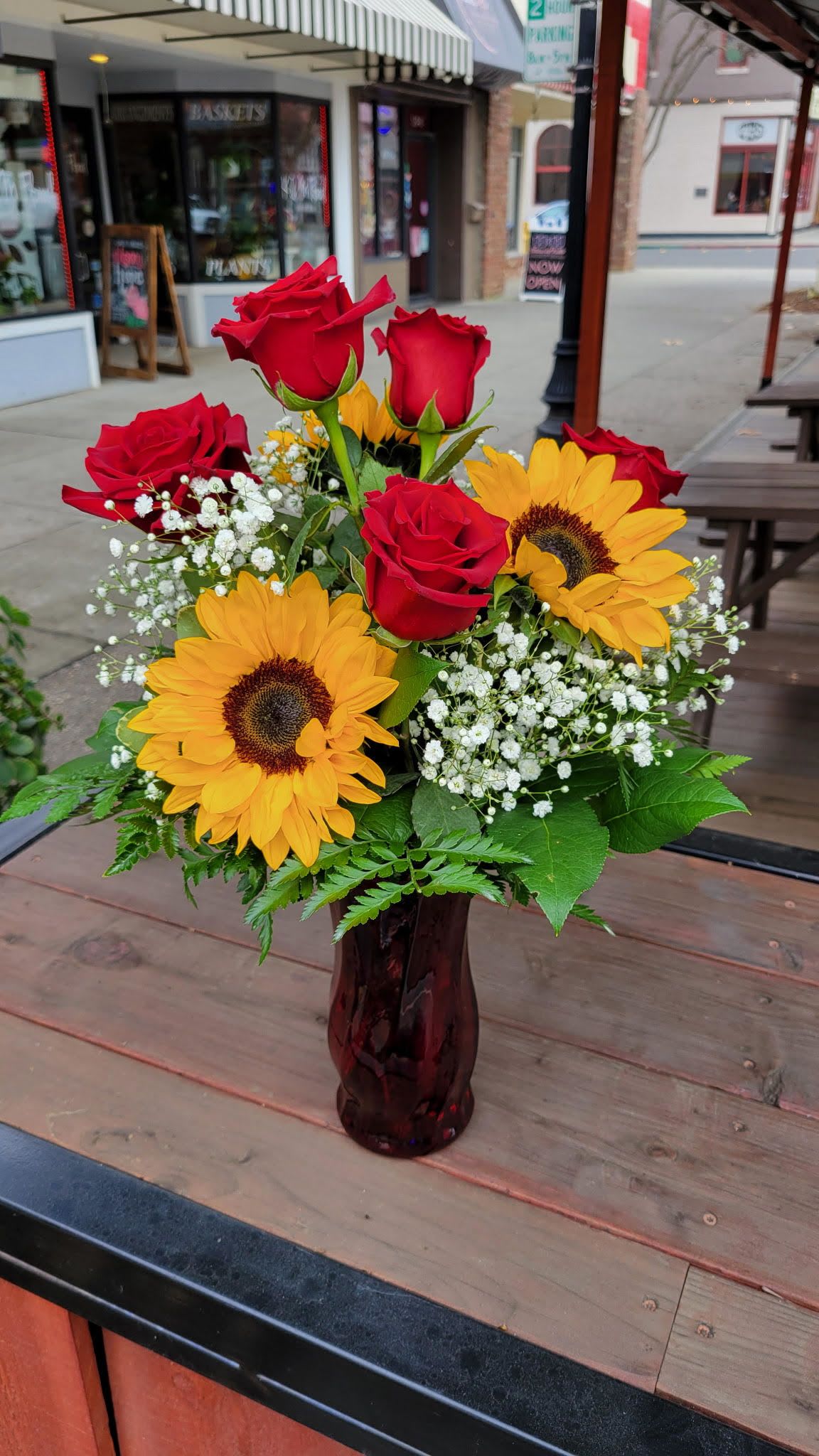 Red roses and yellow sunflowers in a dark glass vase