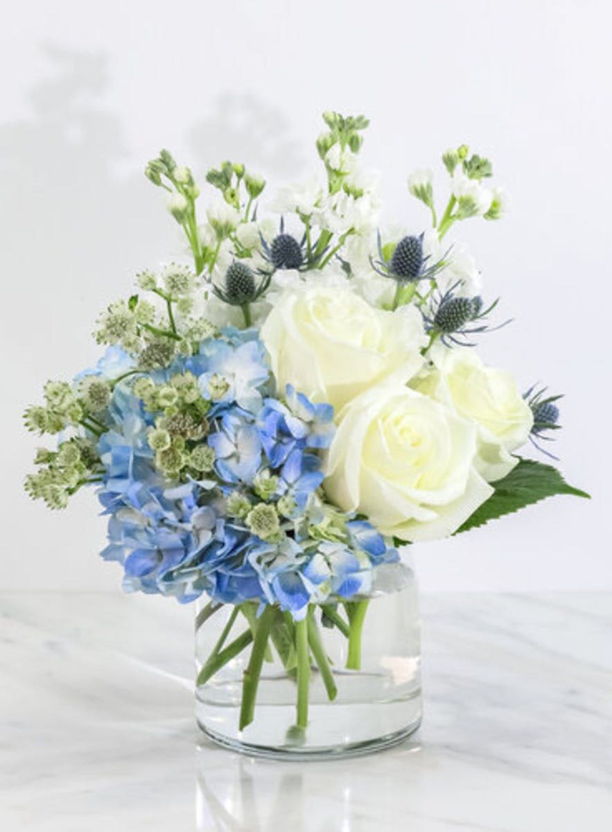 Blue hydrangeas and white roses in a clear glass vase