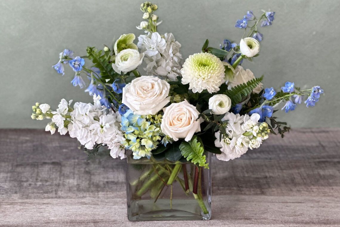 White and blue mixed flower arrangement in a square glass vase