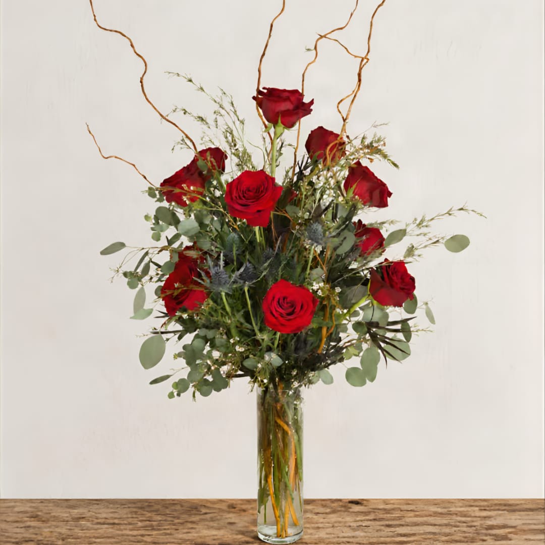 Red roses arranged in a tall glass vase with airy greenery