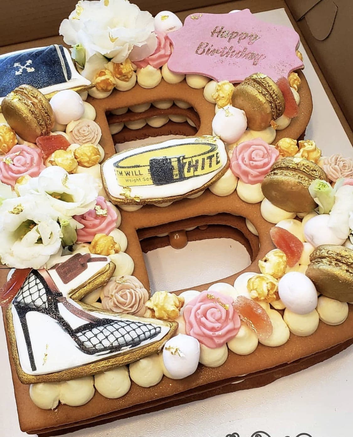 Decorated number-shaped cake with flowers, macarons, and birthday plaques