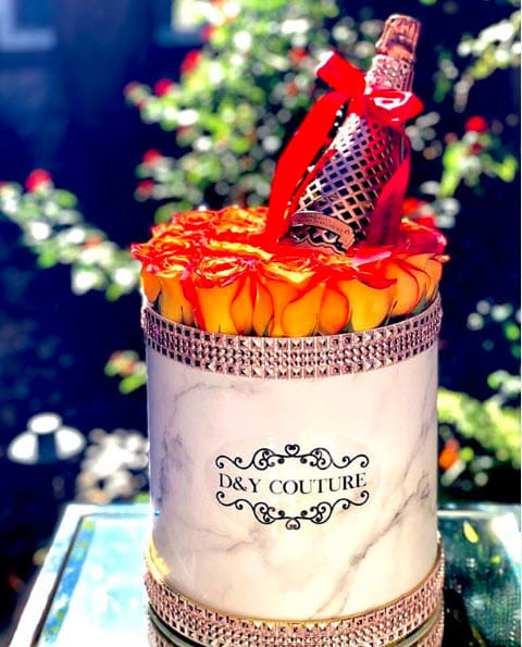Round box of orange roses with a decorative bottle on top