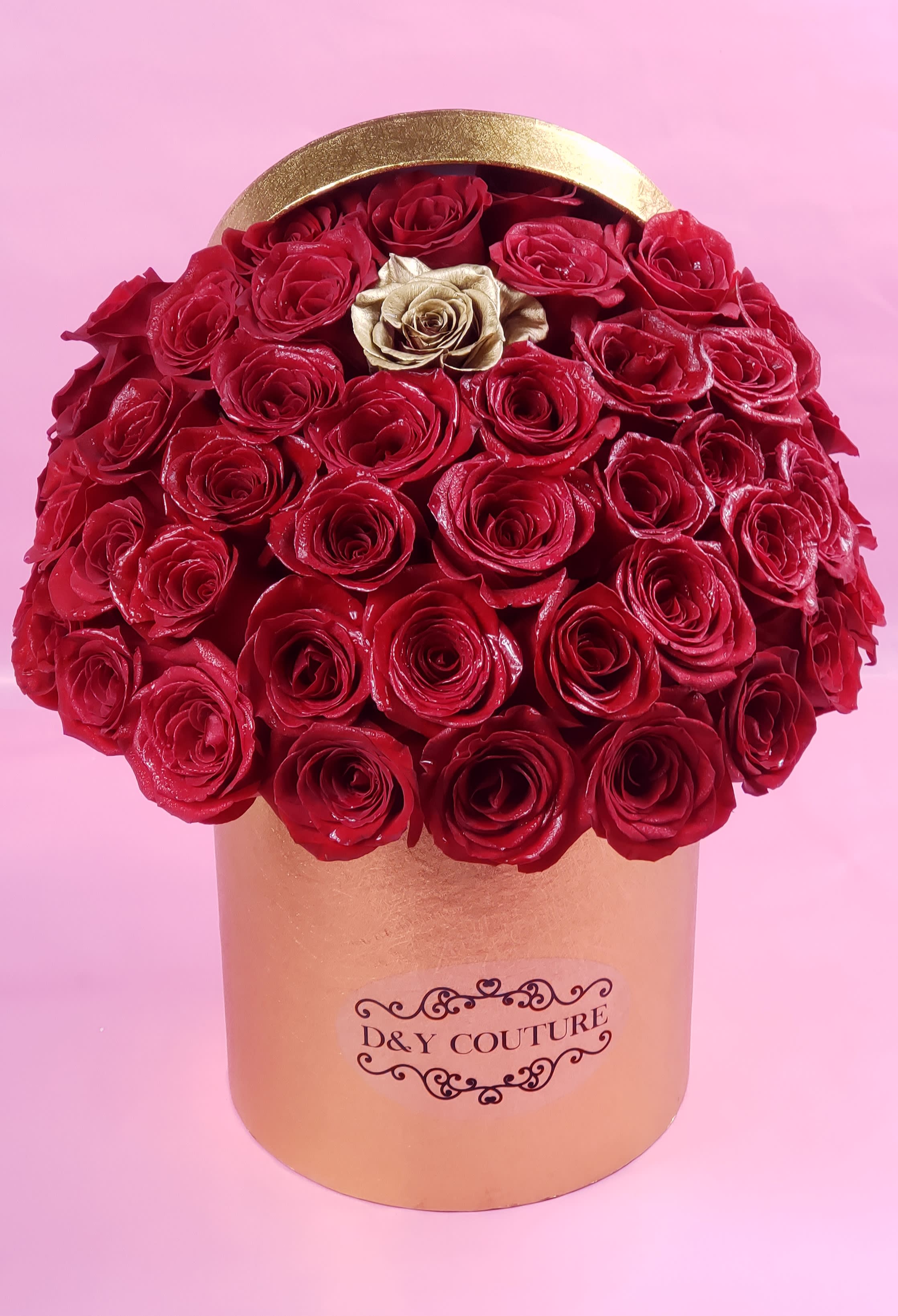 Red roses arranged in a gold round box with one gold rose