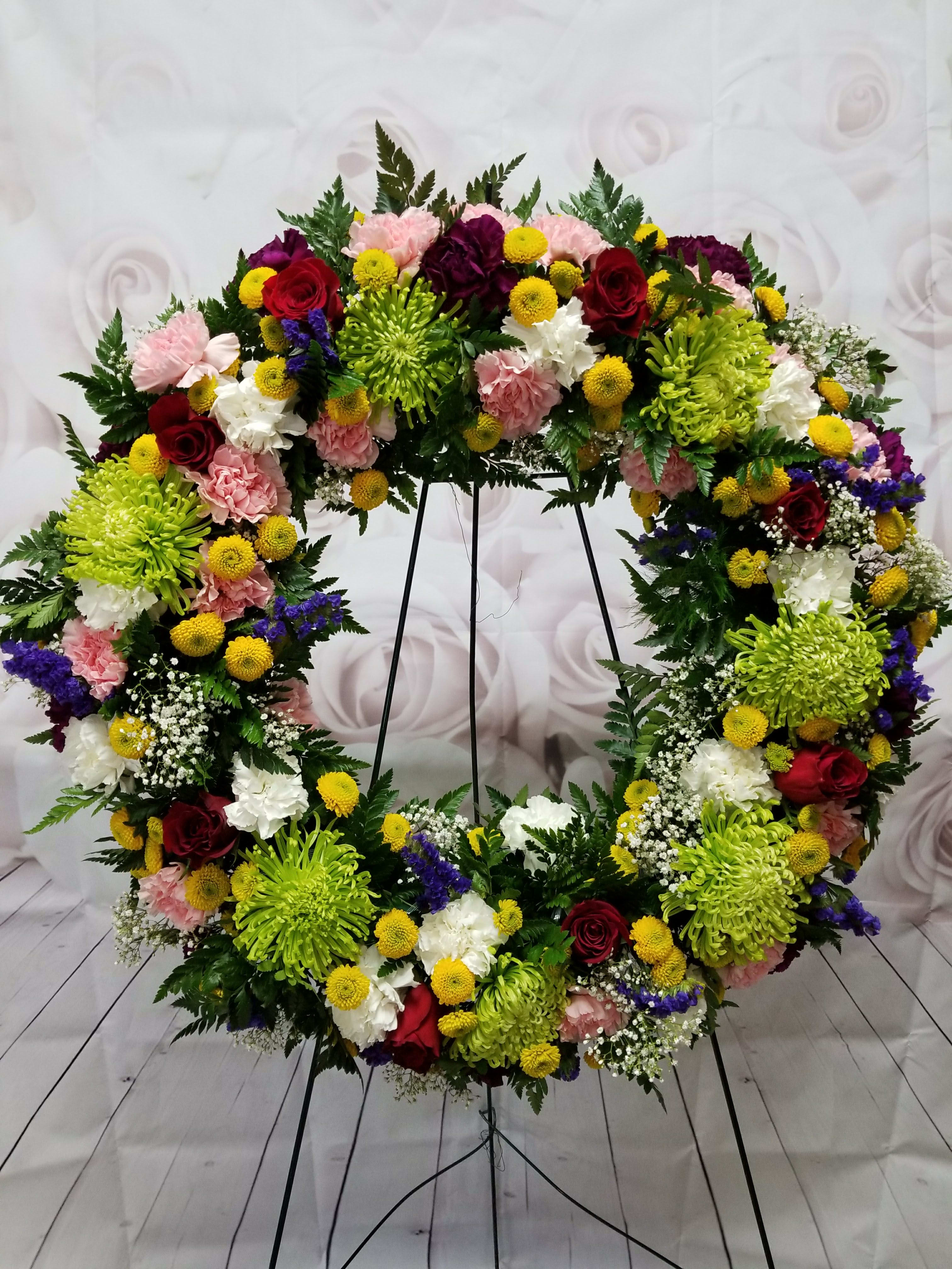 Large floral wreath on a stand with red, pink, white, and yellow blooms
