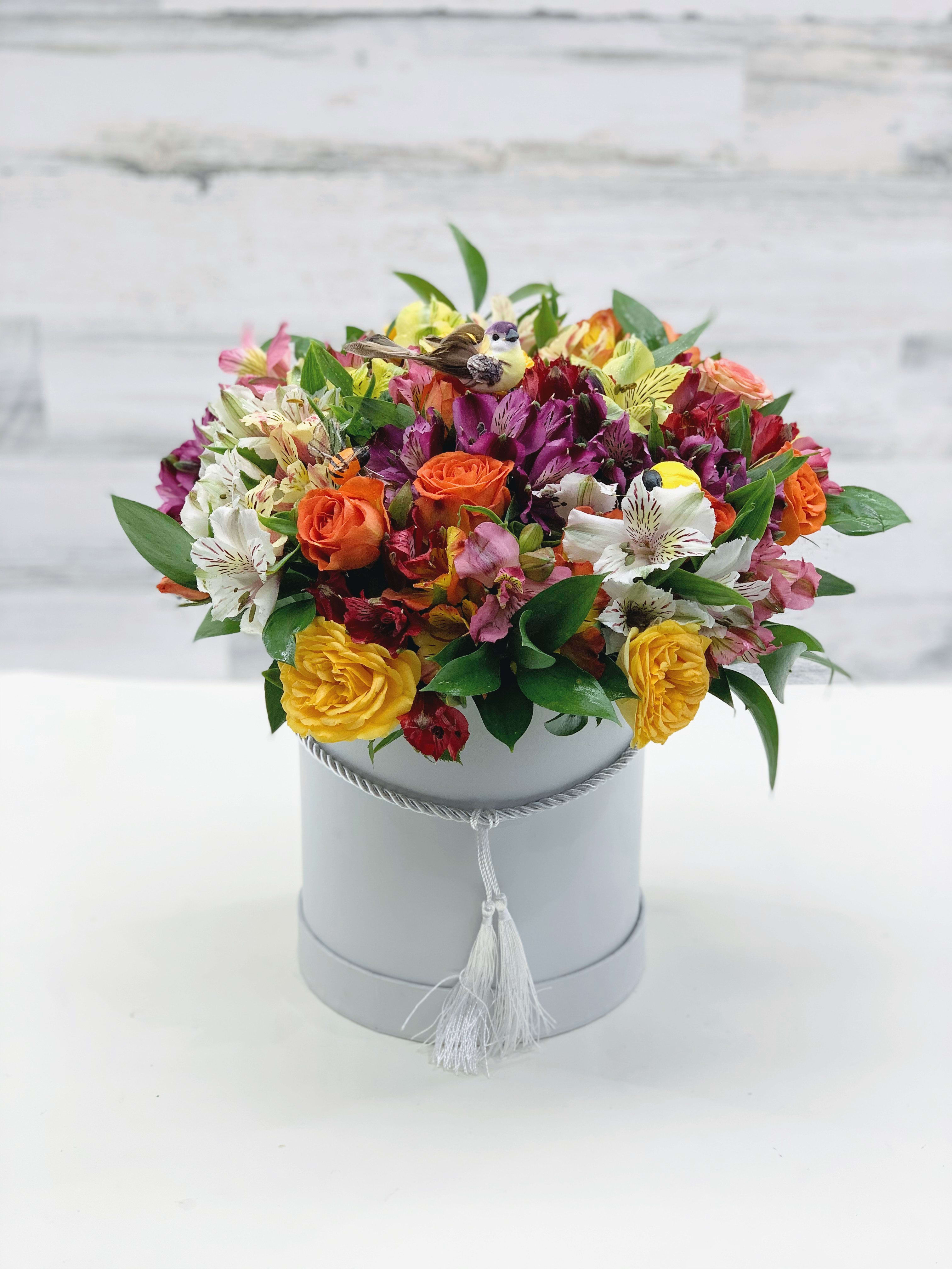 Mixed bouquet of orange, yellow, pink, and white flowers in a gray hat box