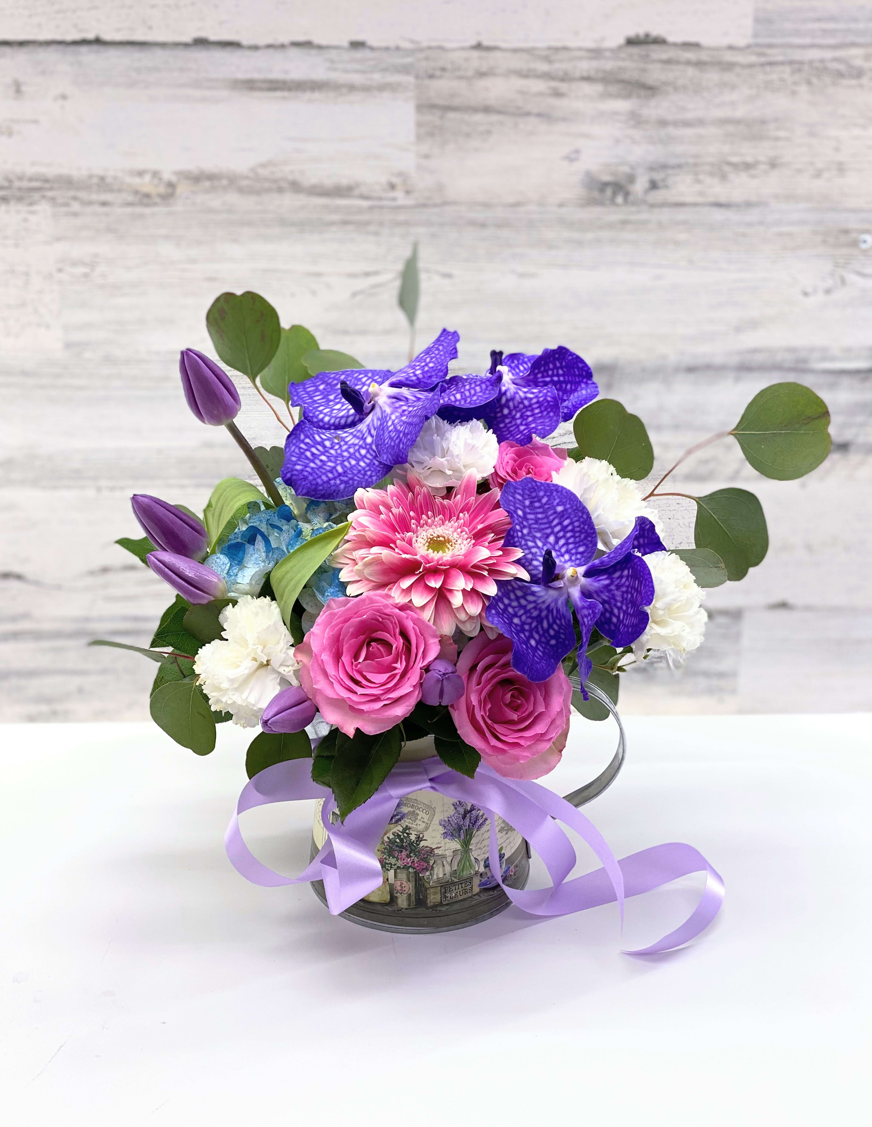 Pink and purple mixed bouquet in a decorative tin container with ribbon
