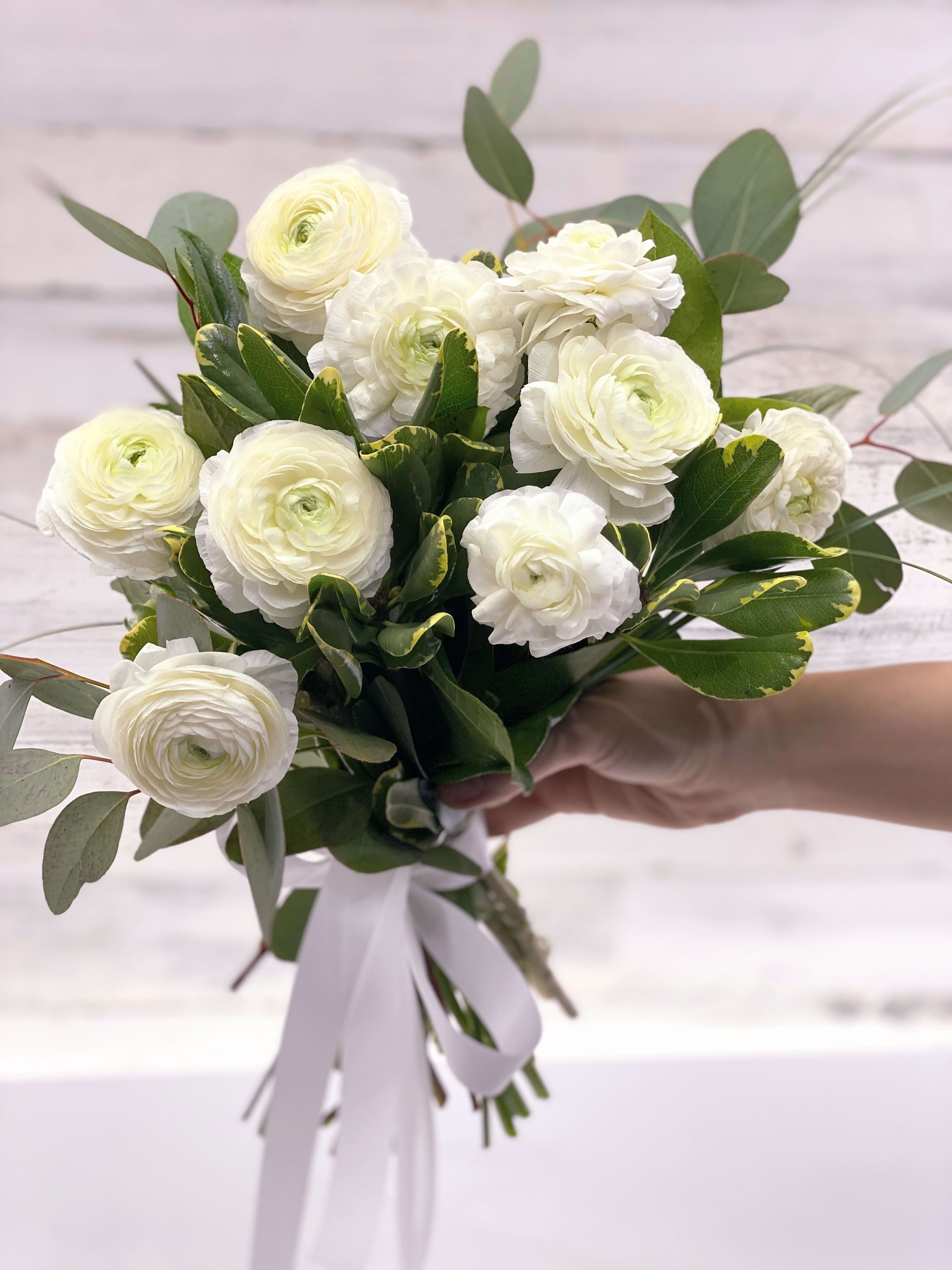White ranunculus bouquet with greenery and a white ribbon