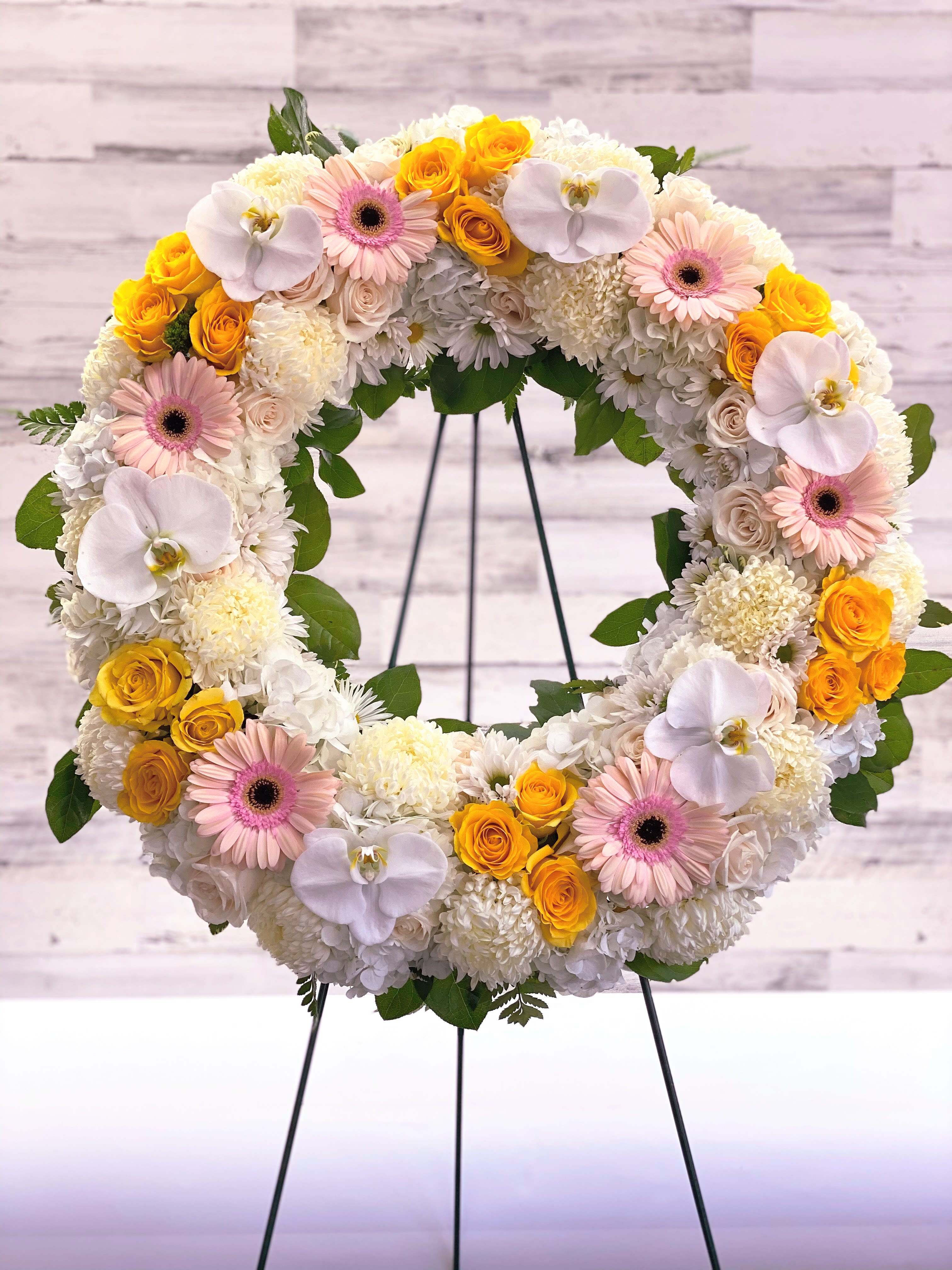 Circular floral wreath with white, pink, and yellow blooms on a stand