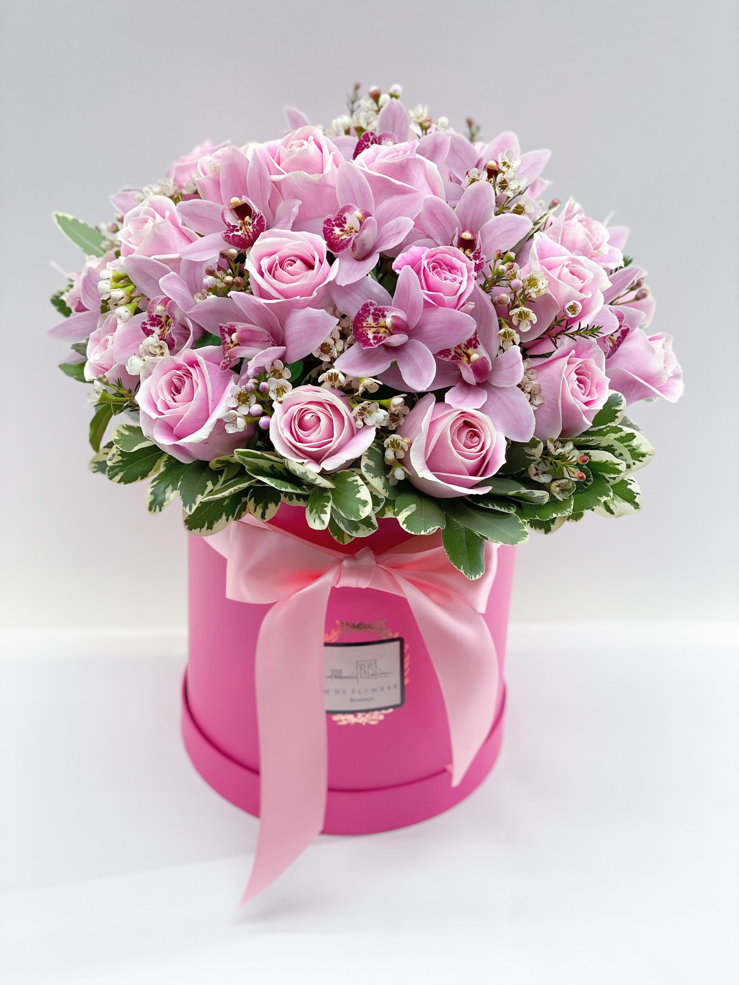 Pink roses and orchids arranged in a round pink box with a ribbon