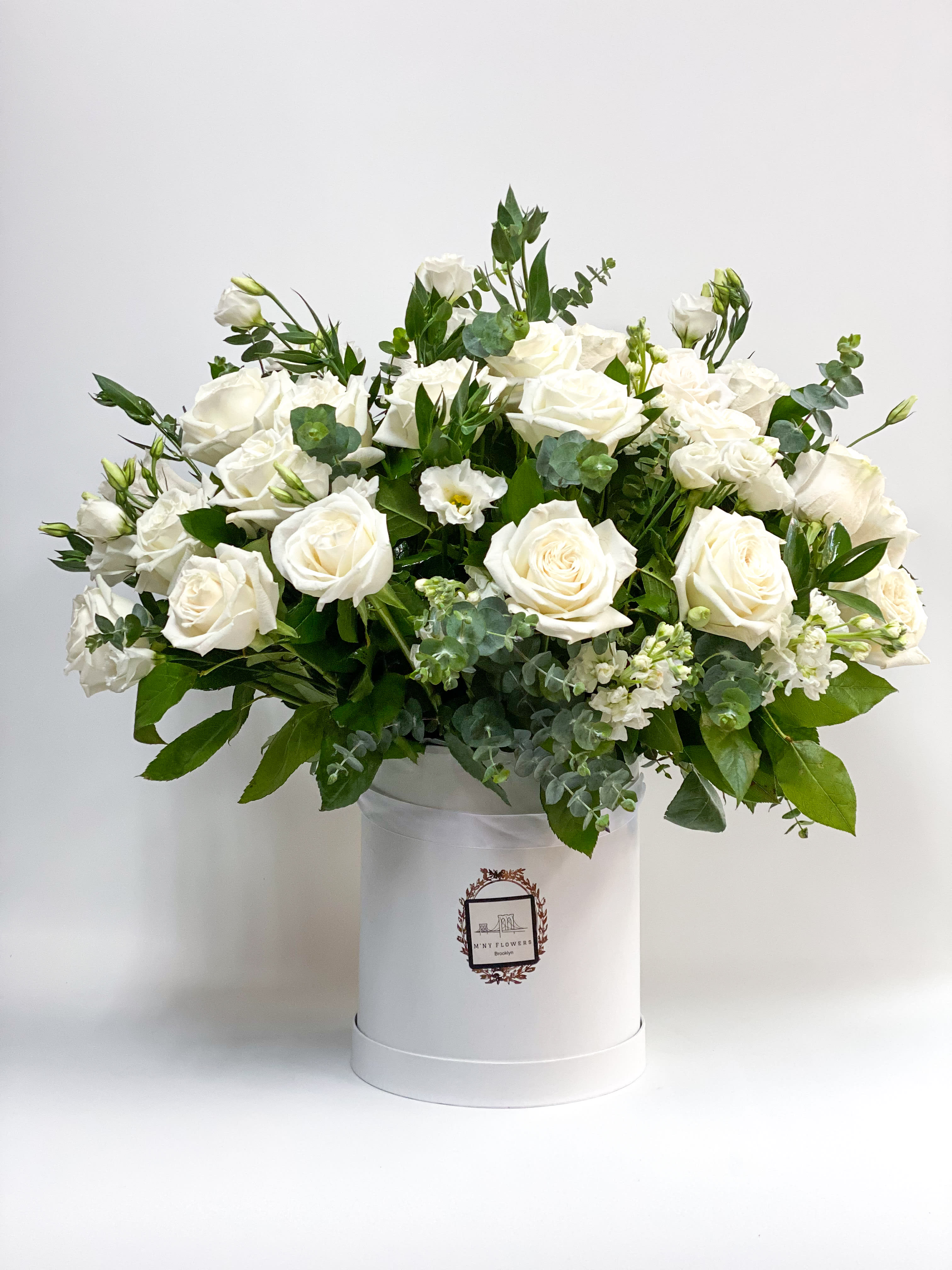 White roses arranged in a white hat box with greenery