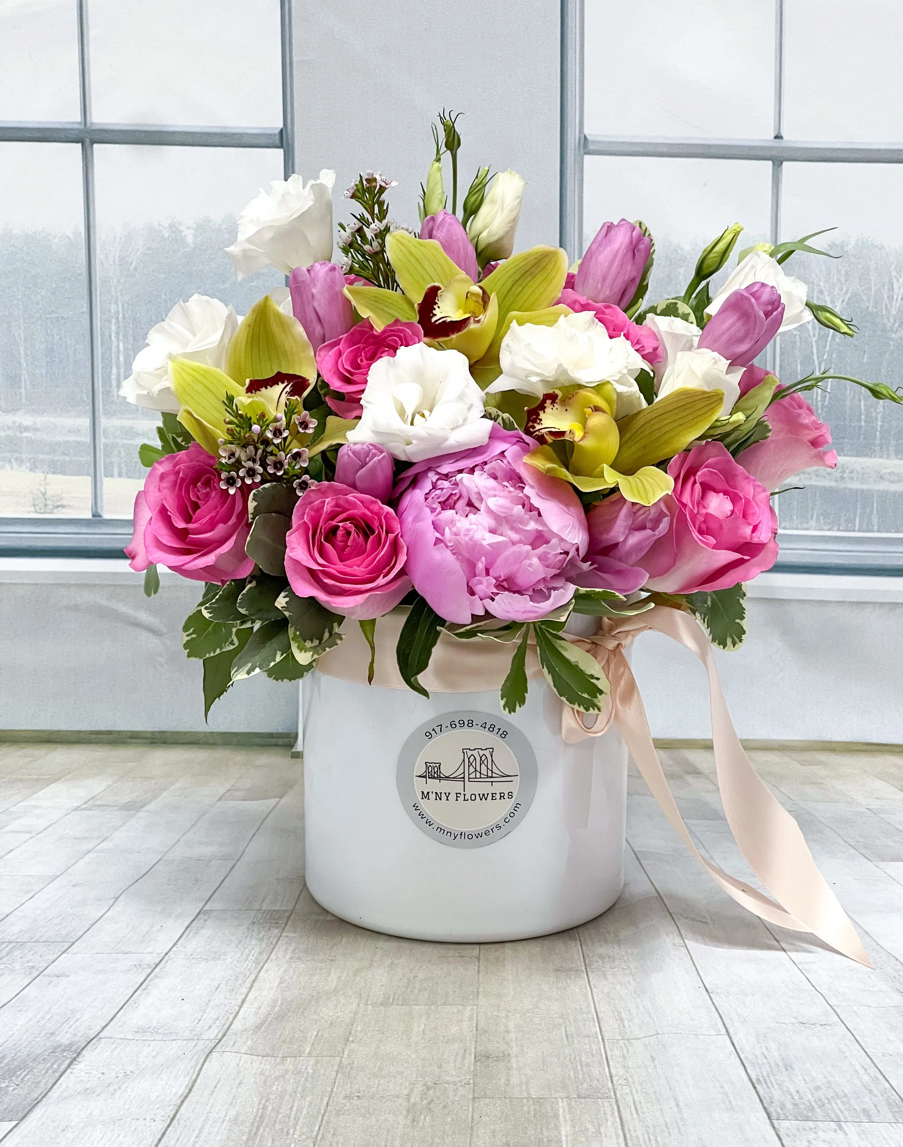 Pink and white flowers arranged in a white hat box with a ribbon