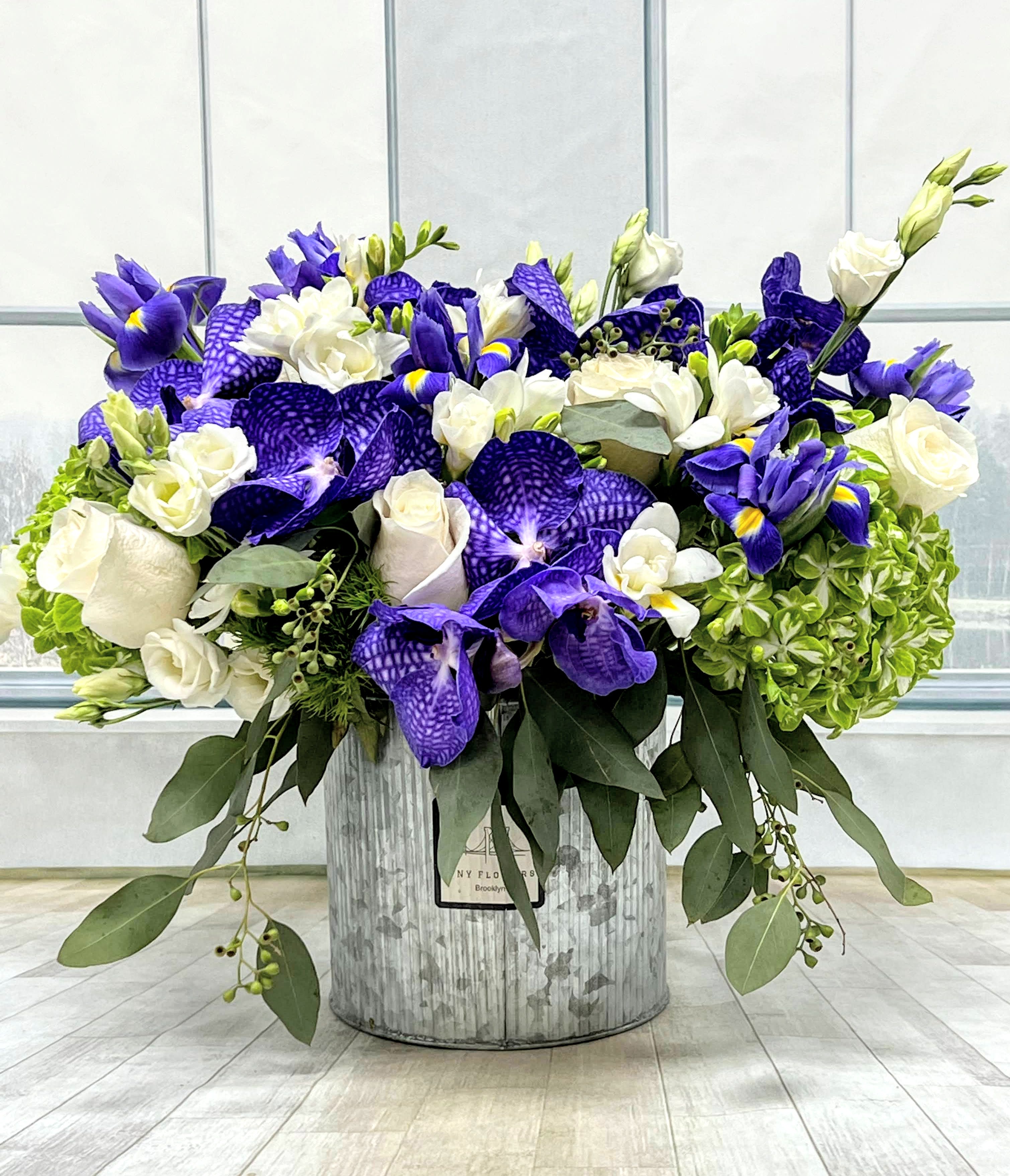 Purple and white floral arrangement in a metal container