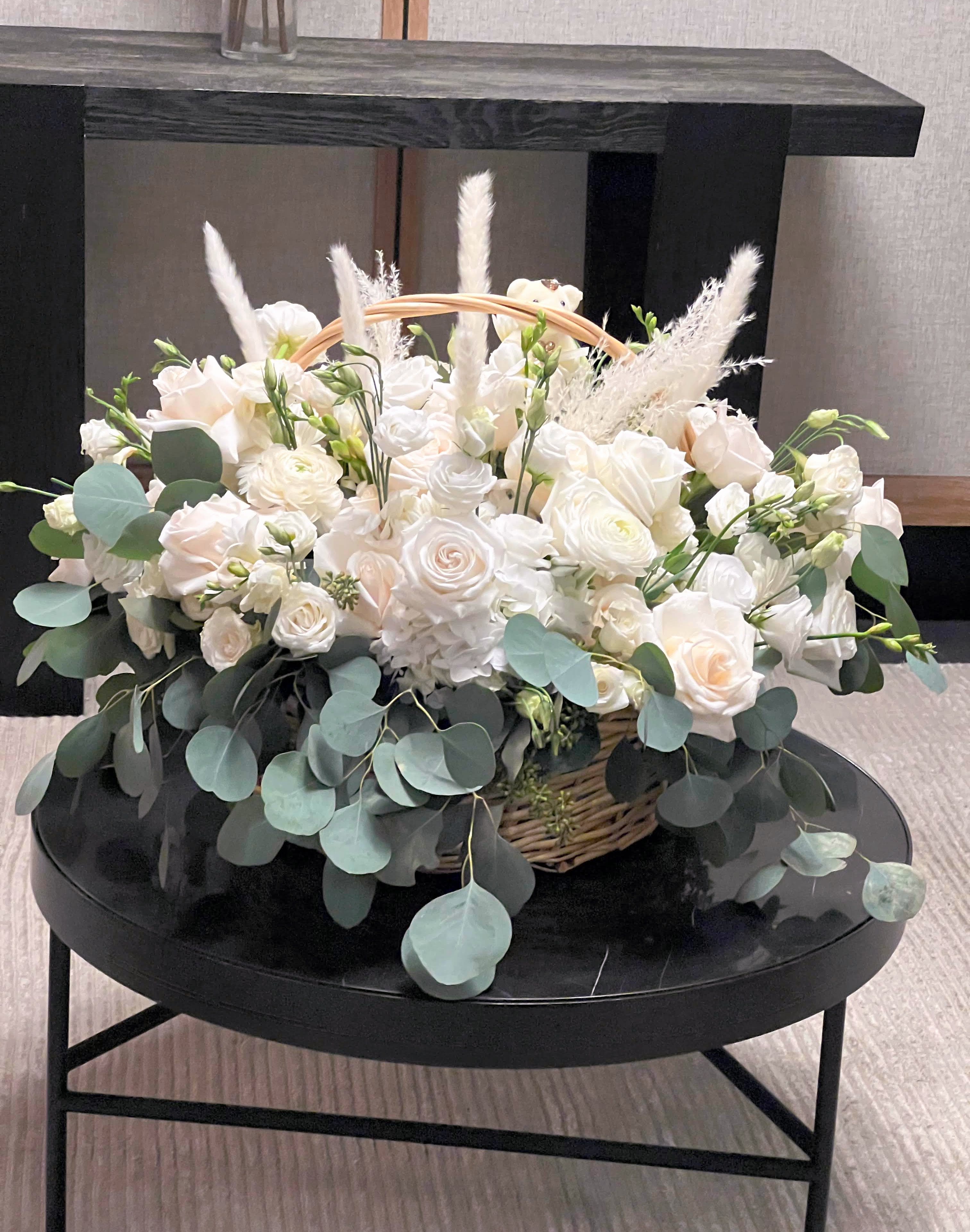 White rose arrangement in a wicker basket with eucalyptus and feathery accents