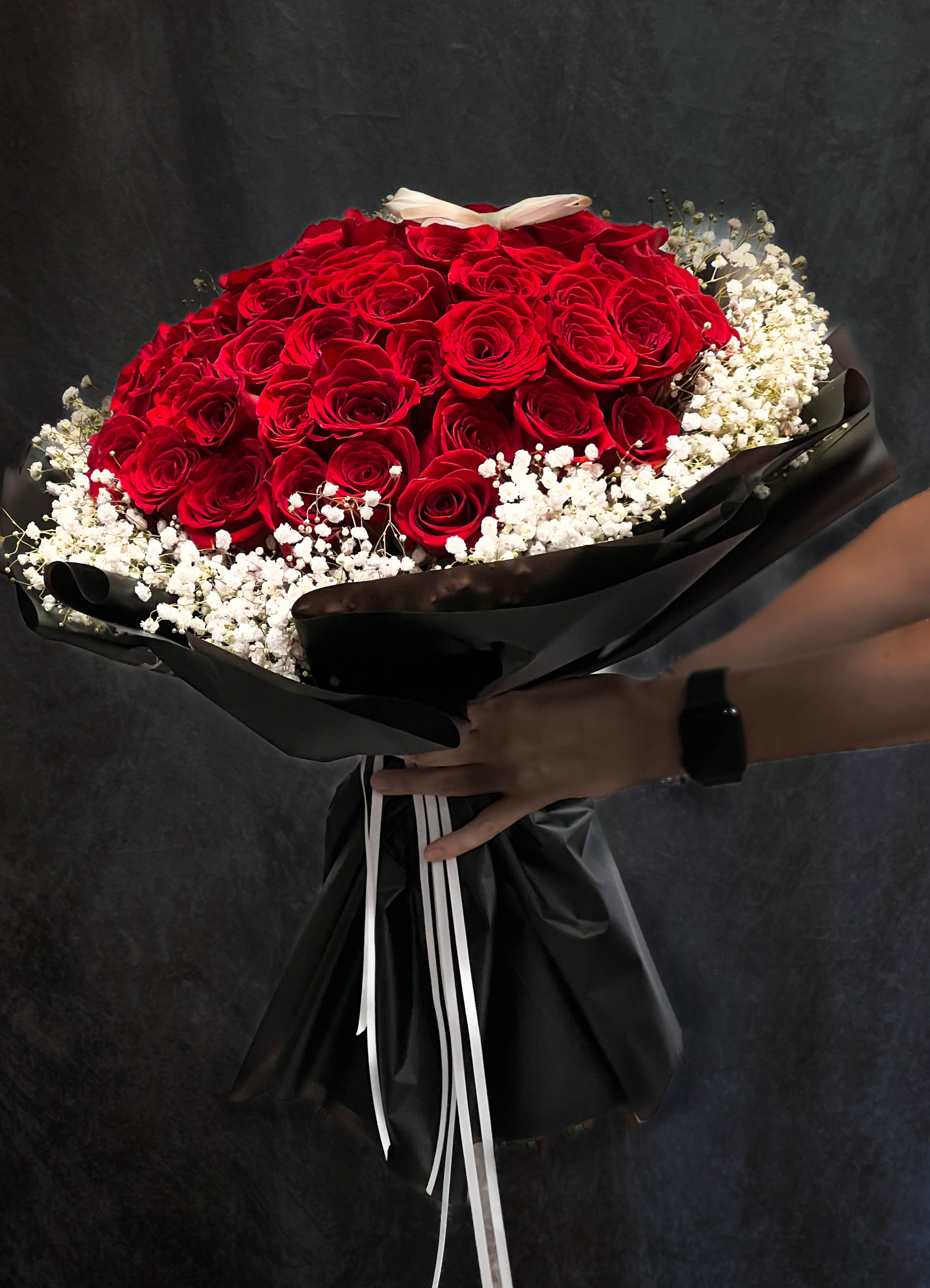 Bouquet of red roses with white baby's breath wrapped in black paper