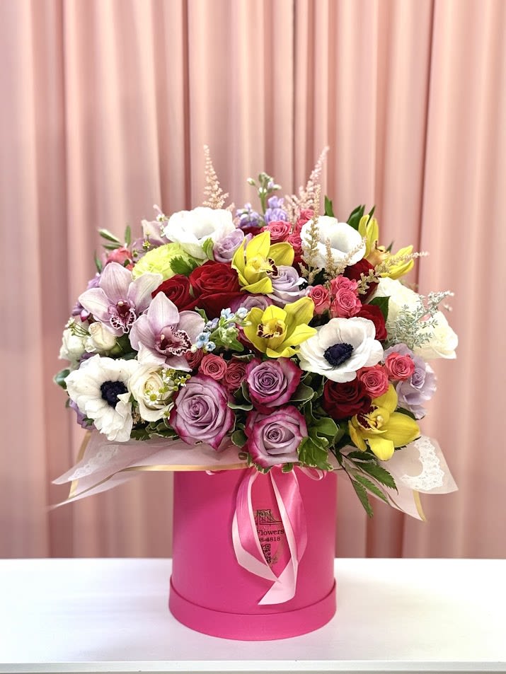 Mixed bouquet of roses, orchids, and anemones in a pink hat box