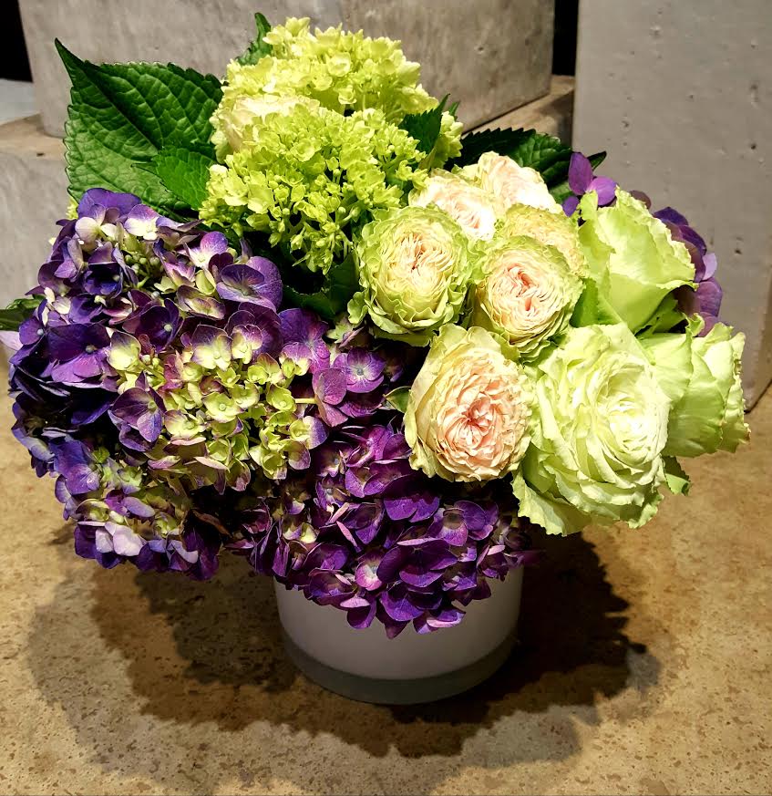 Purple hydrangeas and pale green roses arranged in a white vase