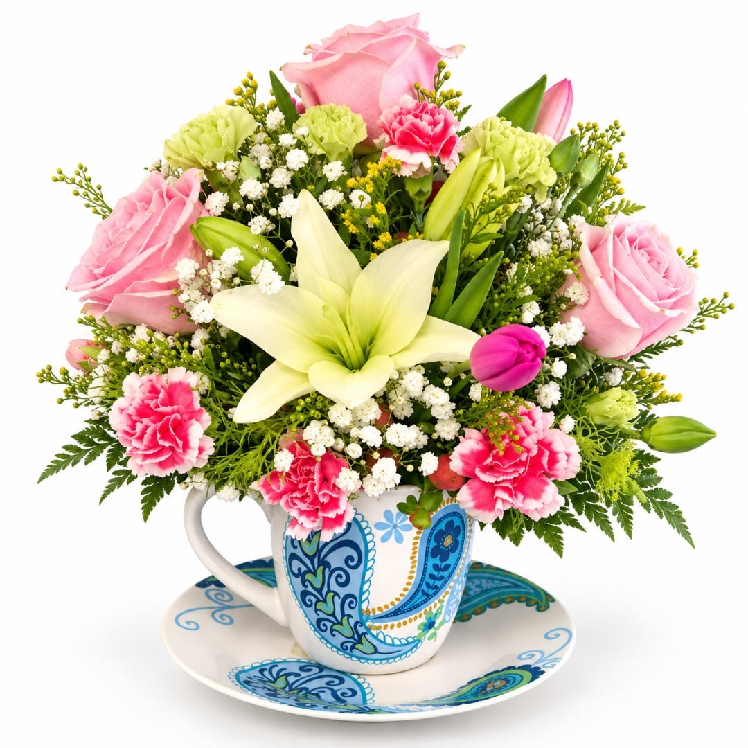 Bouquet of pink roses, lilies, and carnations in a patterned teacup on a matching saucer.