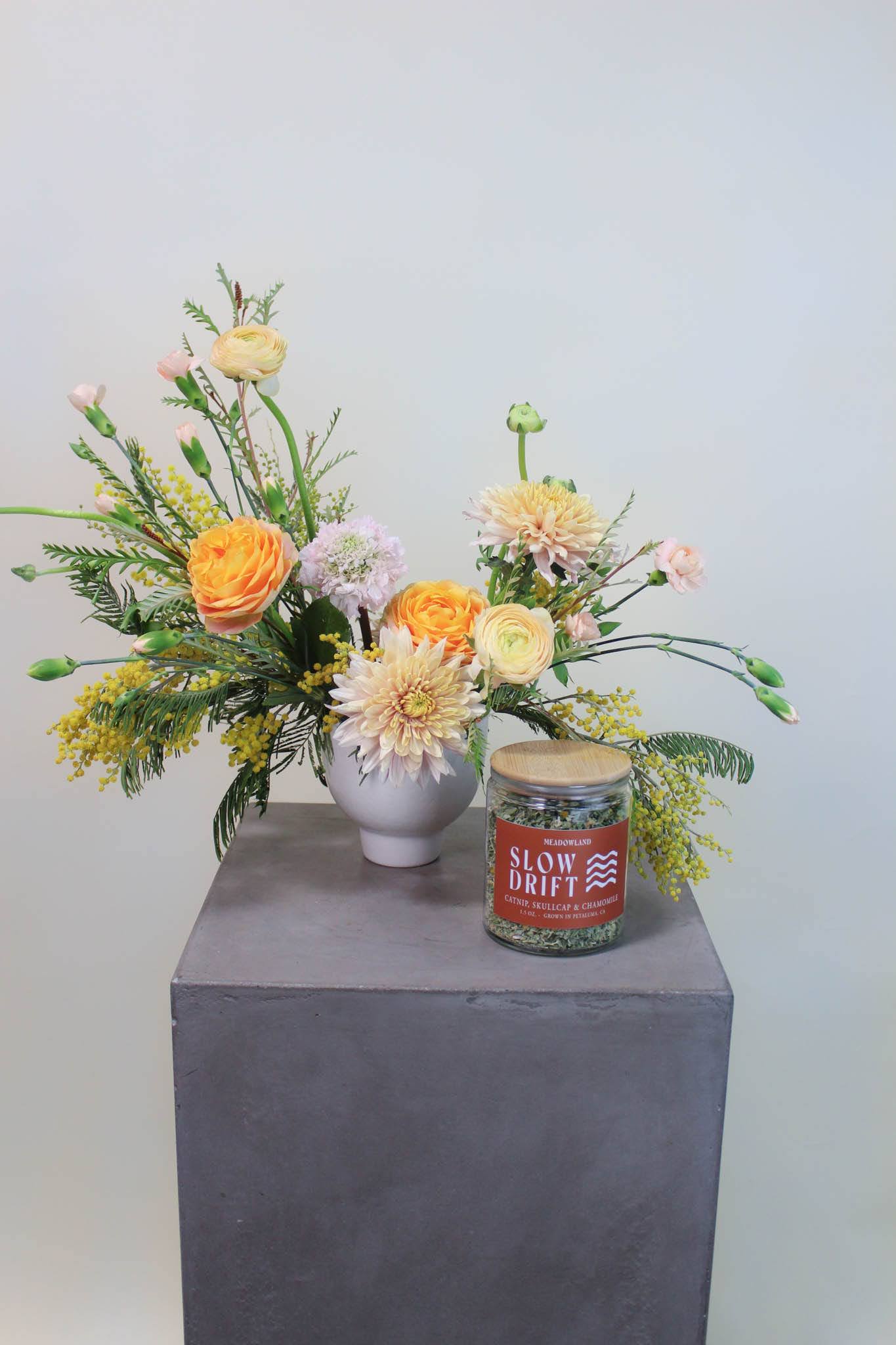 Mixed floral arrangement in a white vase with a jar candle beside it