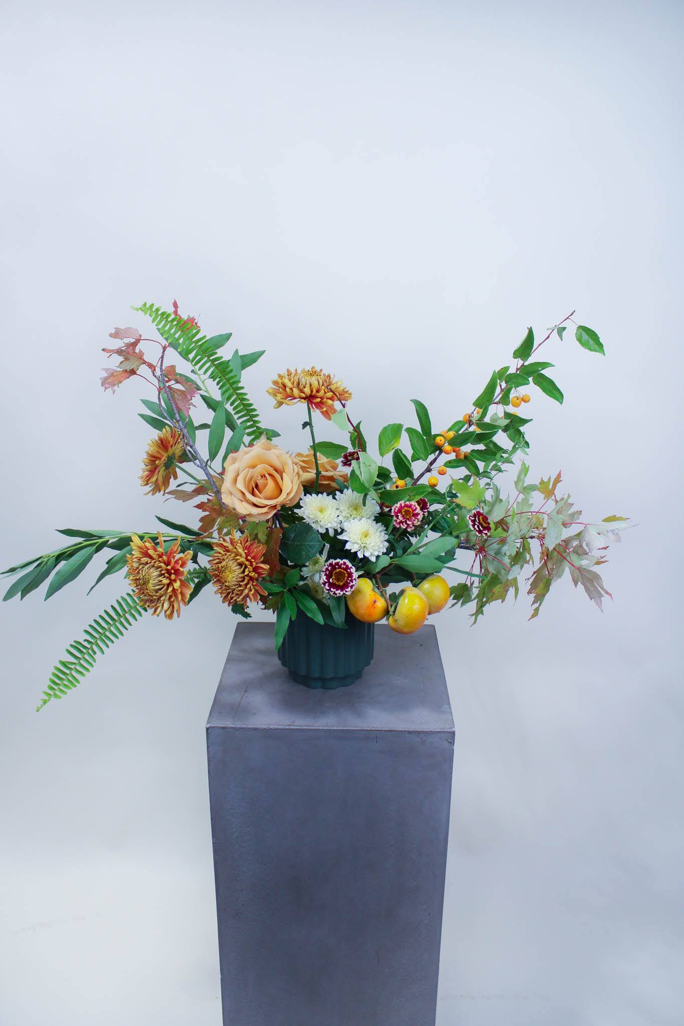 Mixed floral arrangement in a dark vase with peach roses and orange chrysanthemums
