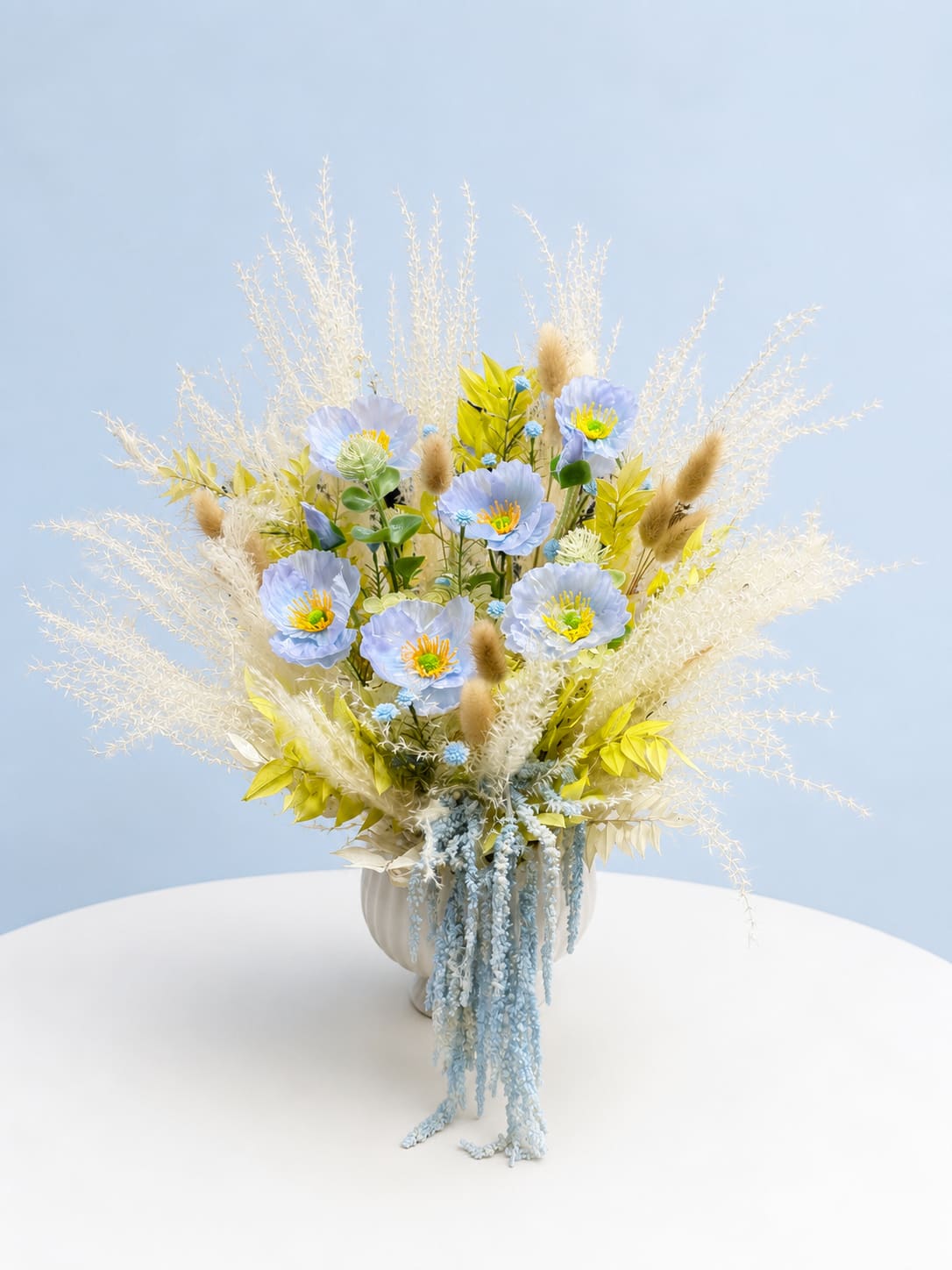 Tall pastel bouquet with blue flowers and dried grasses in a white vase