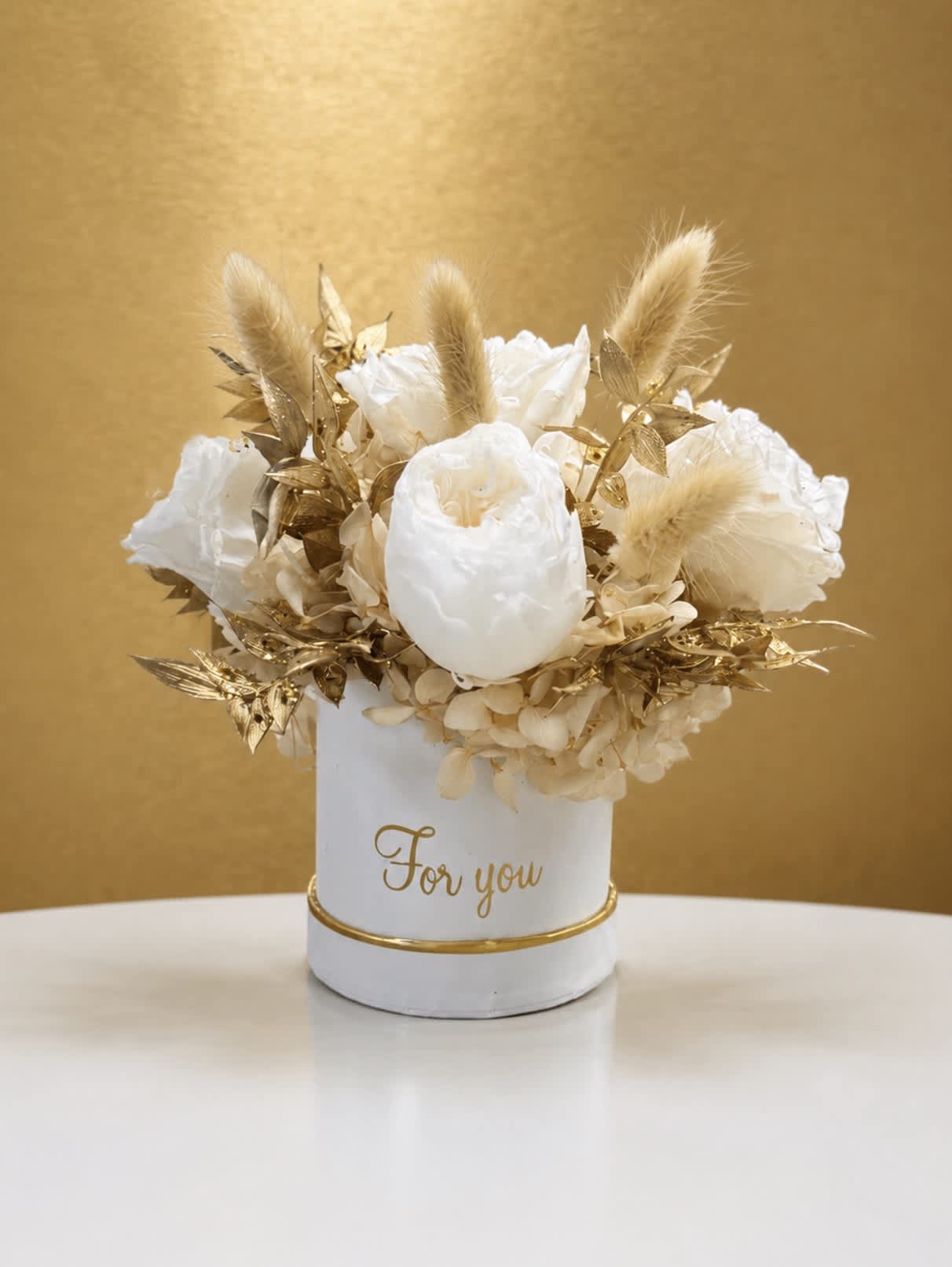 White floral arrangement in a white container with gold accents