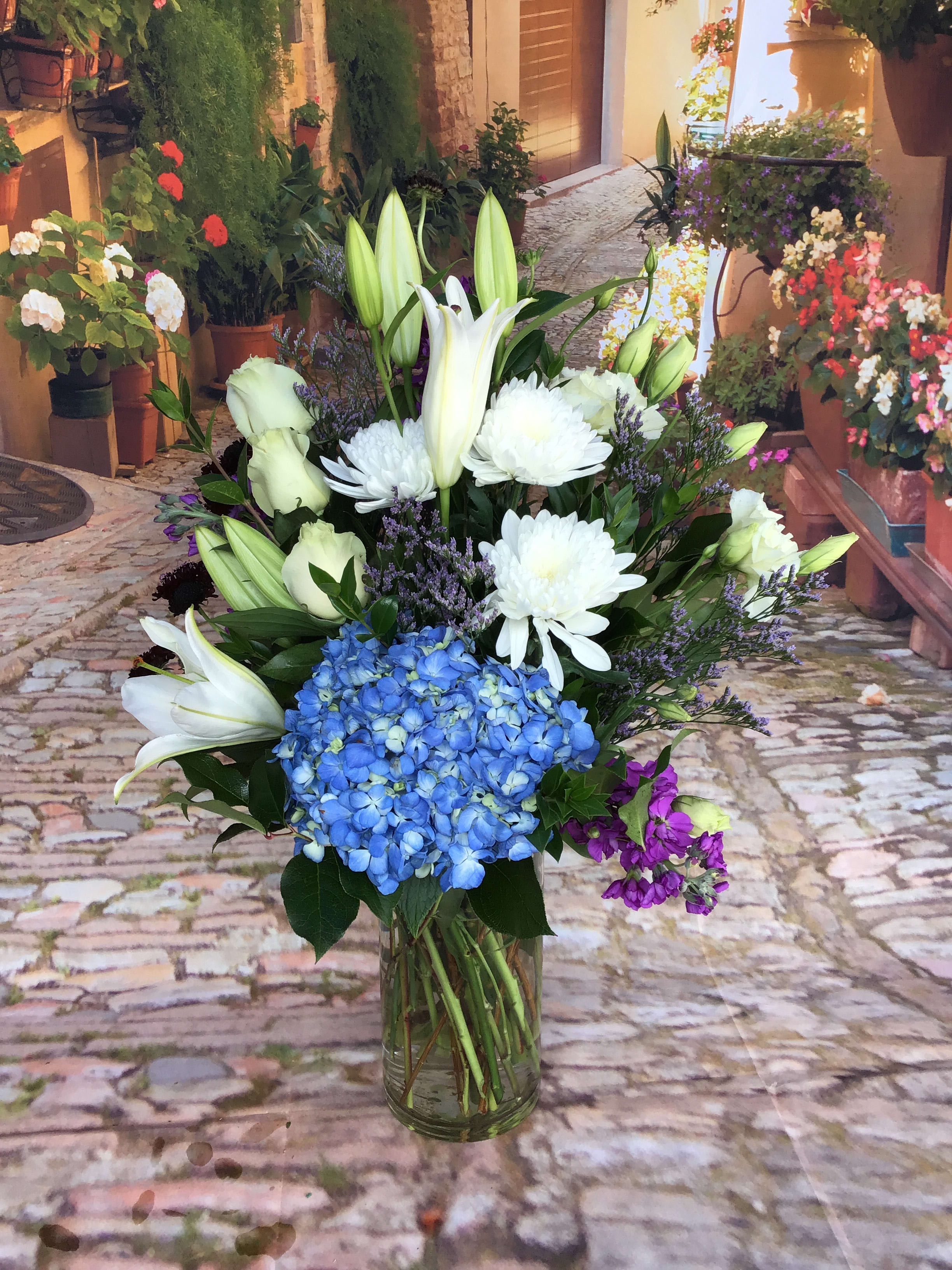 Bouquet of white lilies, blue hydrangea, and white chrysanthemums in a glass vase